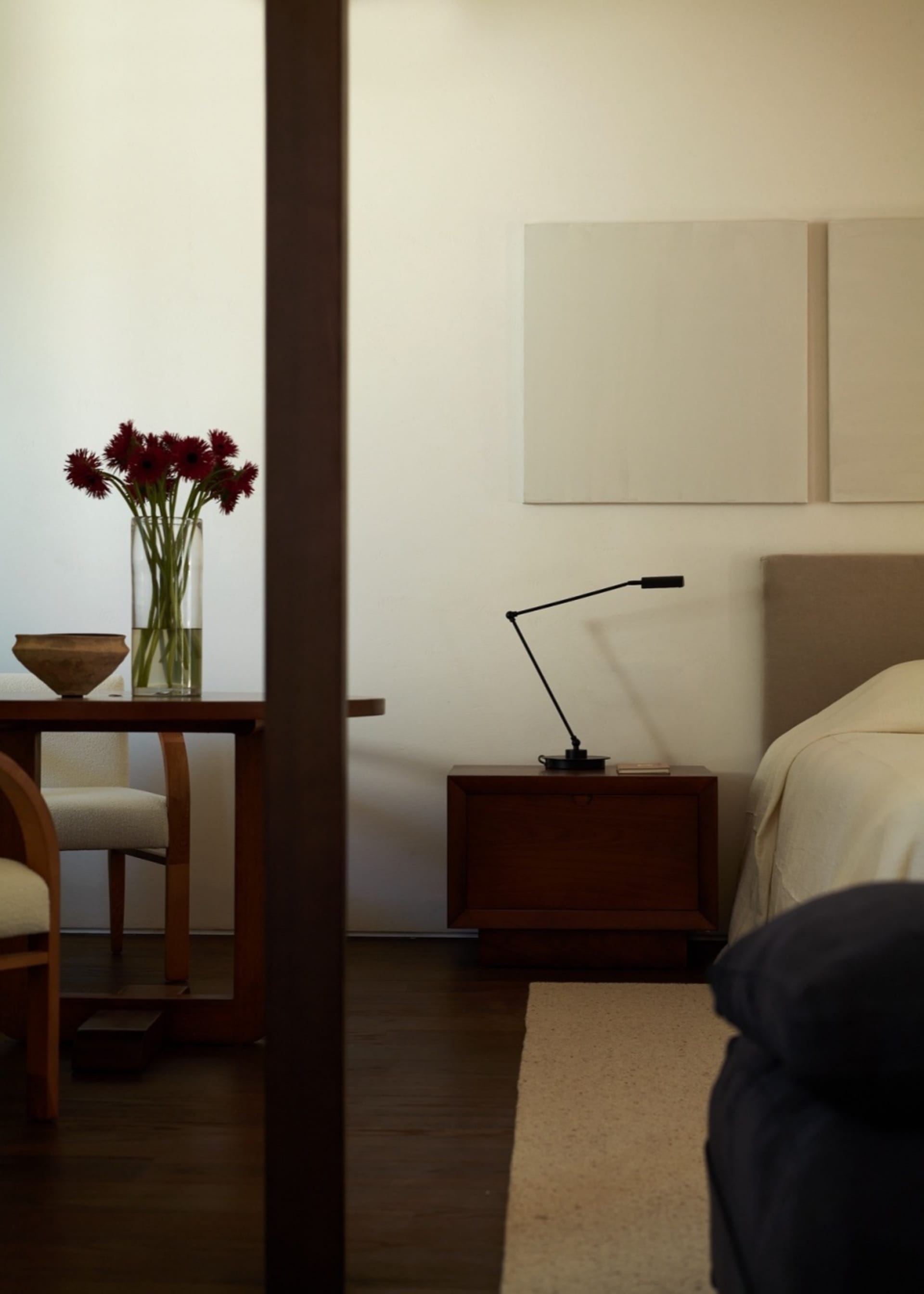 Modern, minimalist bedroom with wooden furniture and a vase of red flowers on a table.