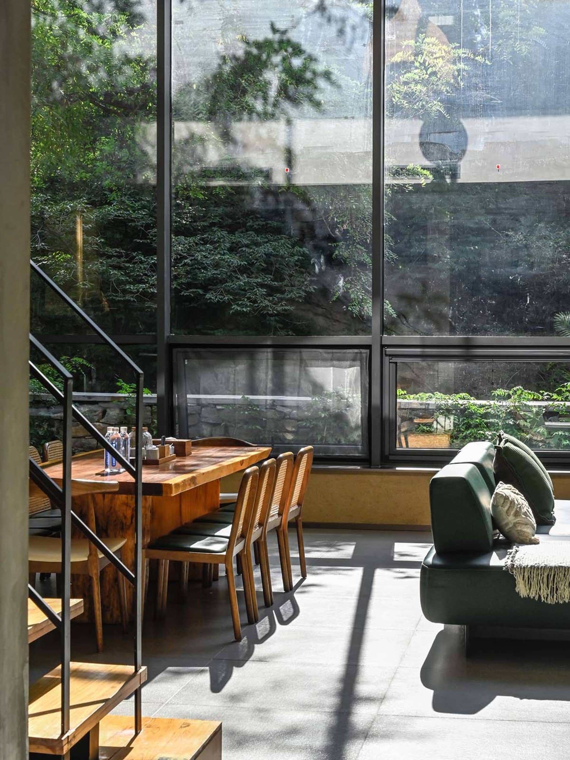 A minimalist living room with wooden furniture, large windows, and a green sofa.