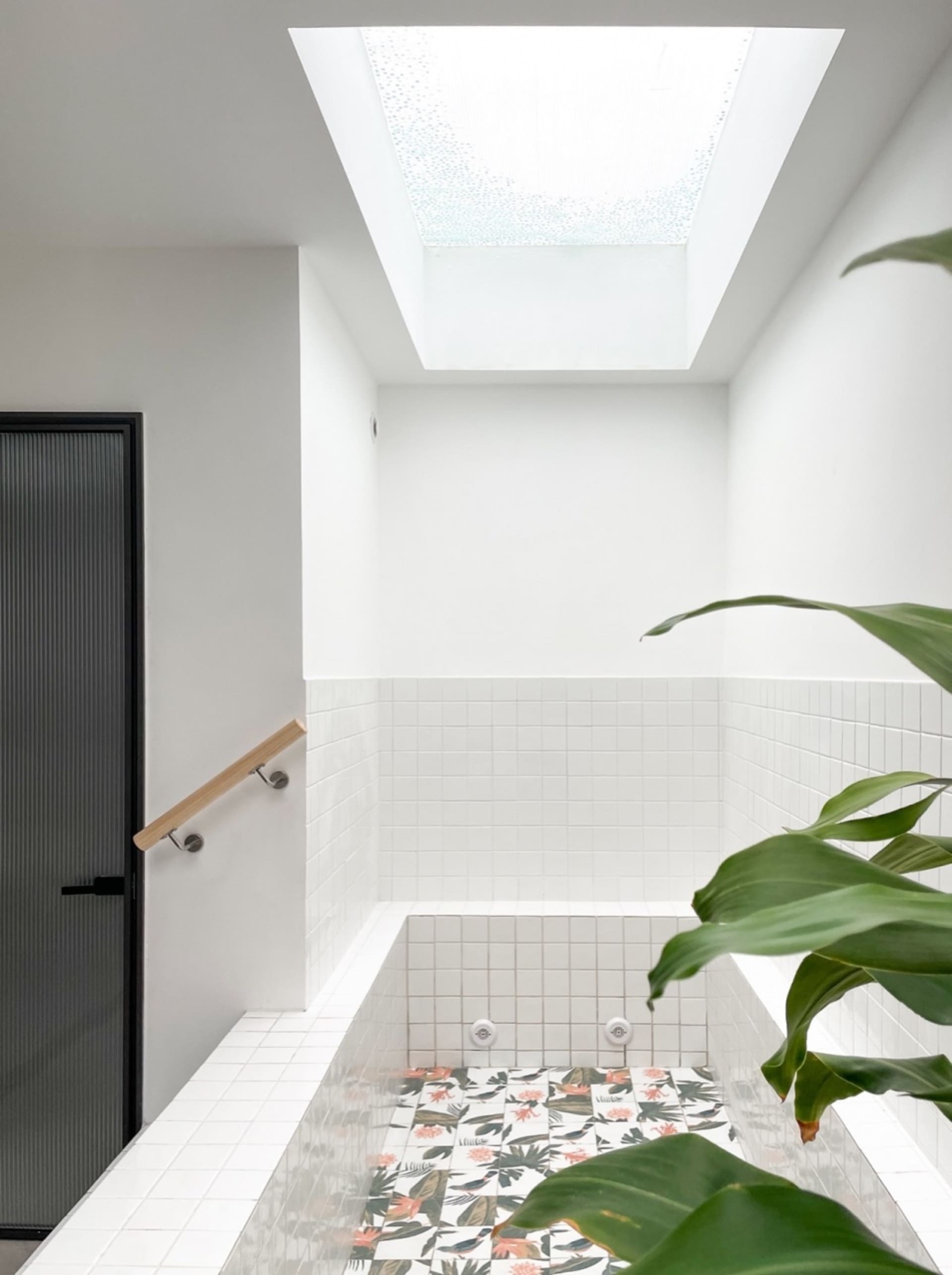 A modern bathroom featuring white tiled walls, a patterned floral tile floor, and a skylight with glass blocks