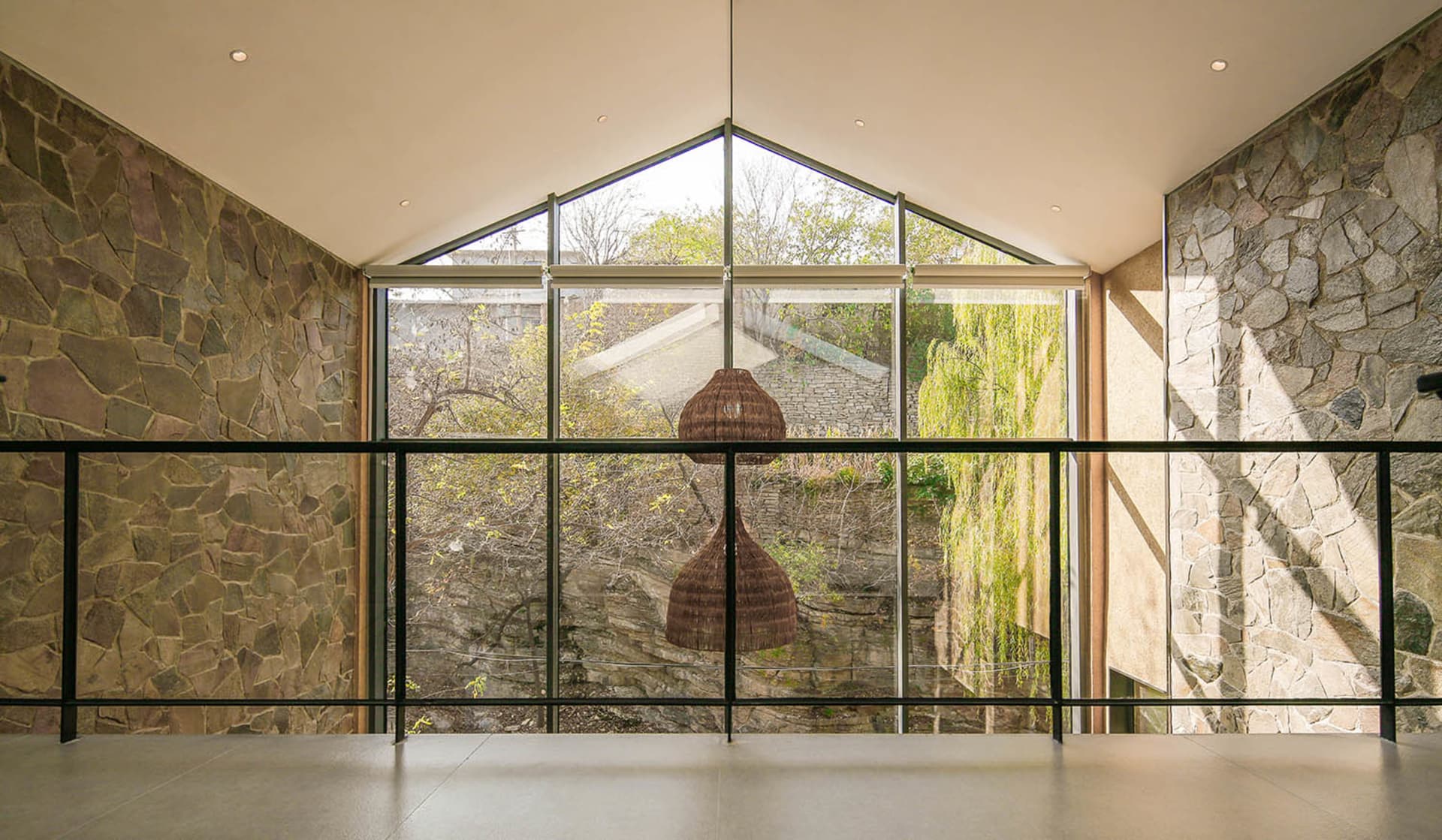 A modern interior design featuring a glass window with a view of trees and a stone wall.