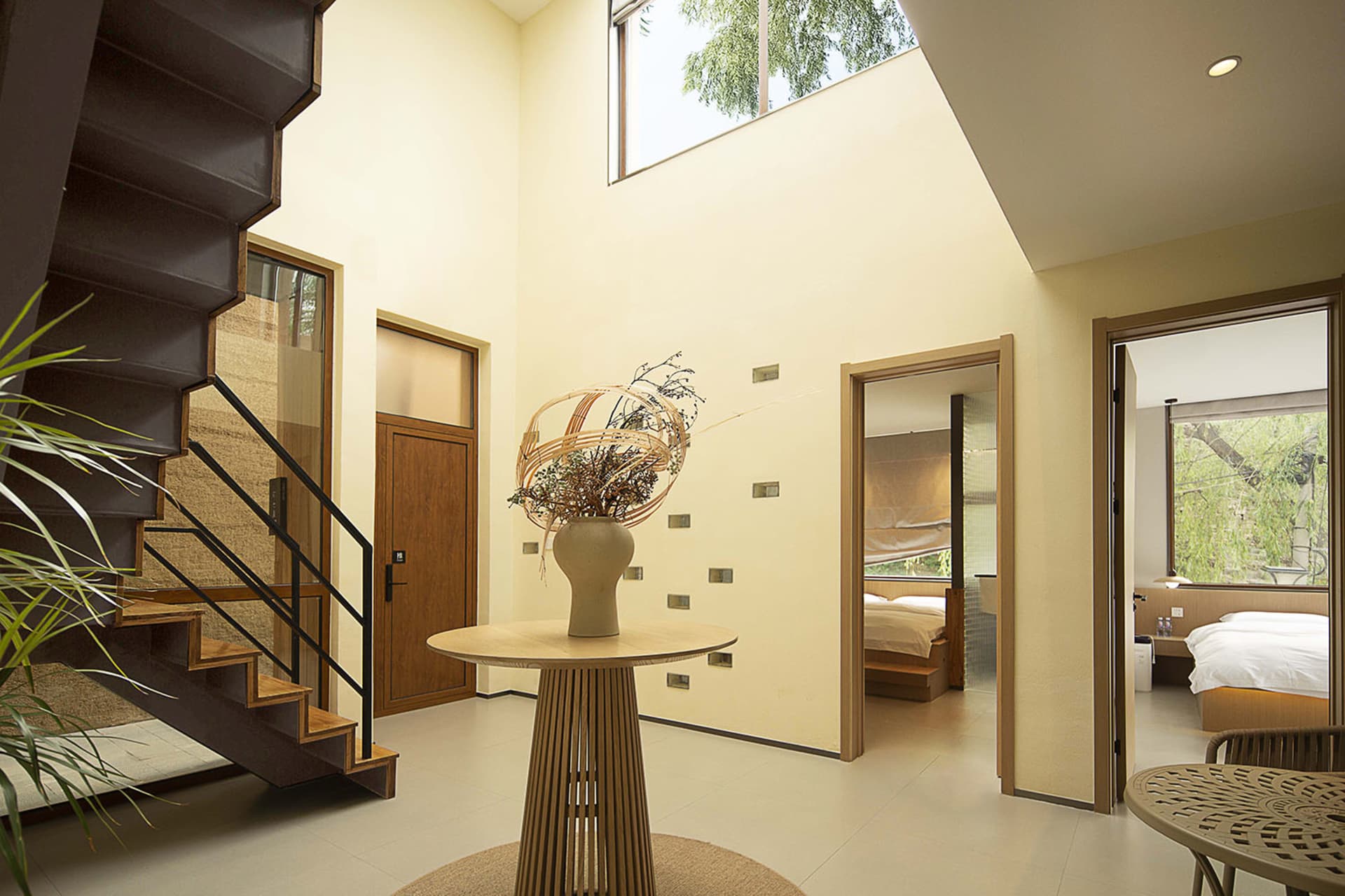 A modern interior space featuring a metallic staircase, natural light, and minimalist design.