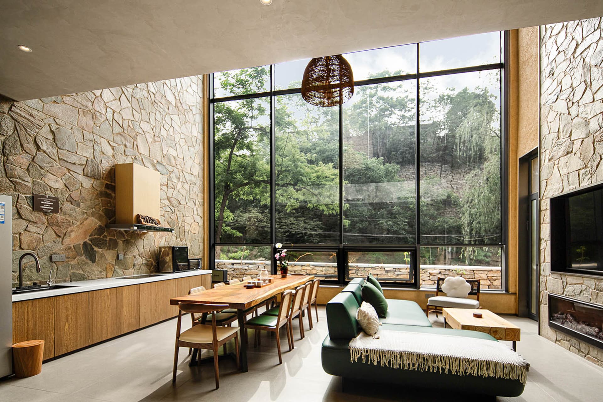 A modern industrial living room with a wooden table and green sofa overlooking a forest.