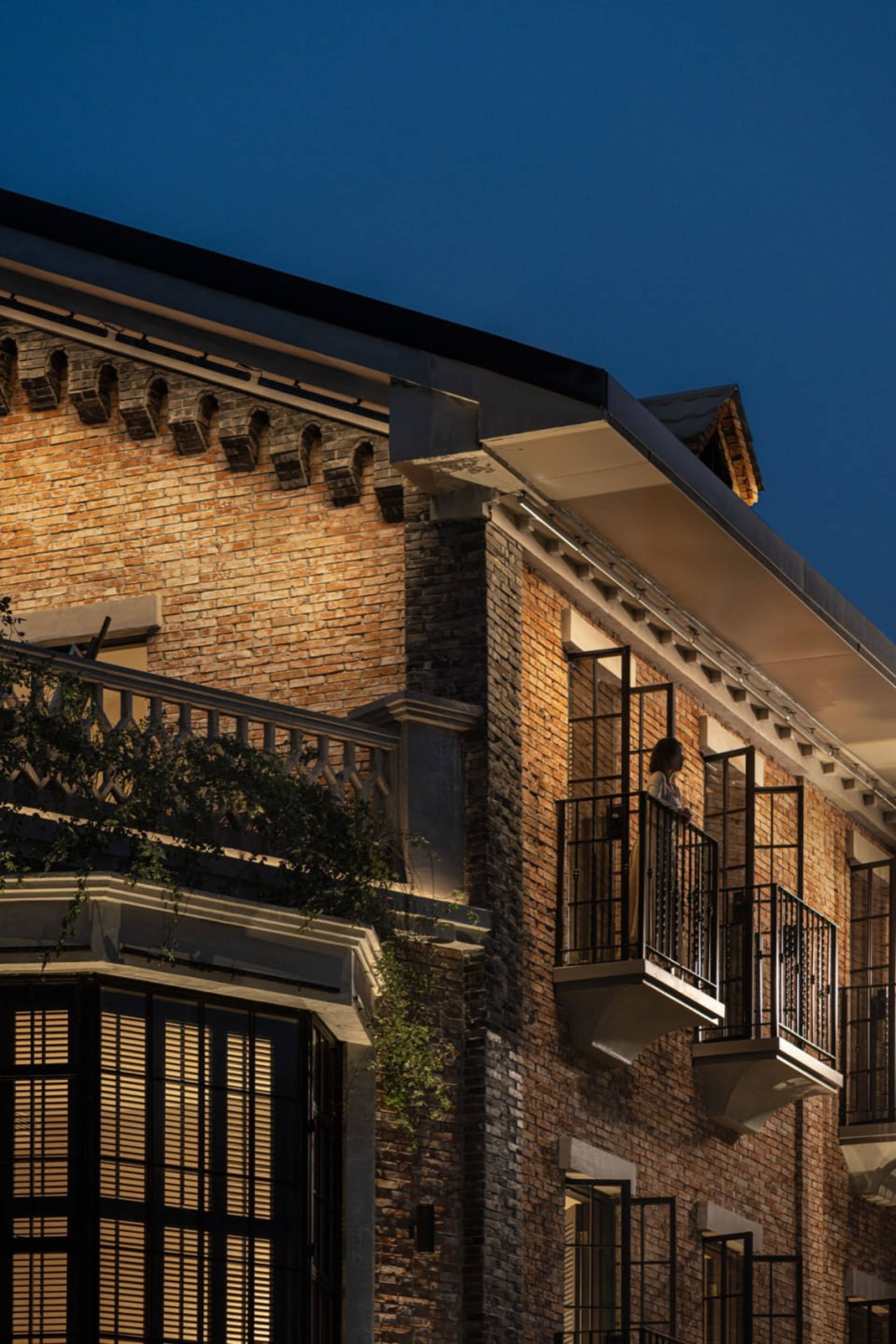 A cozy brick building at night with a person standing on a balcony