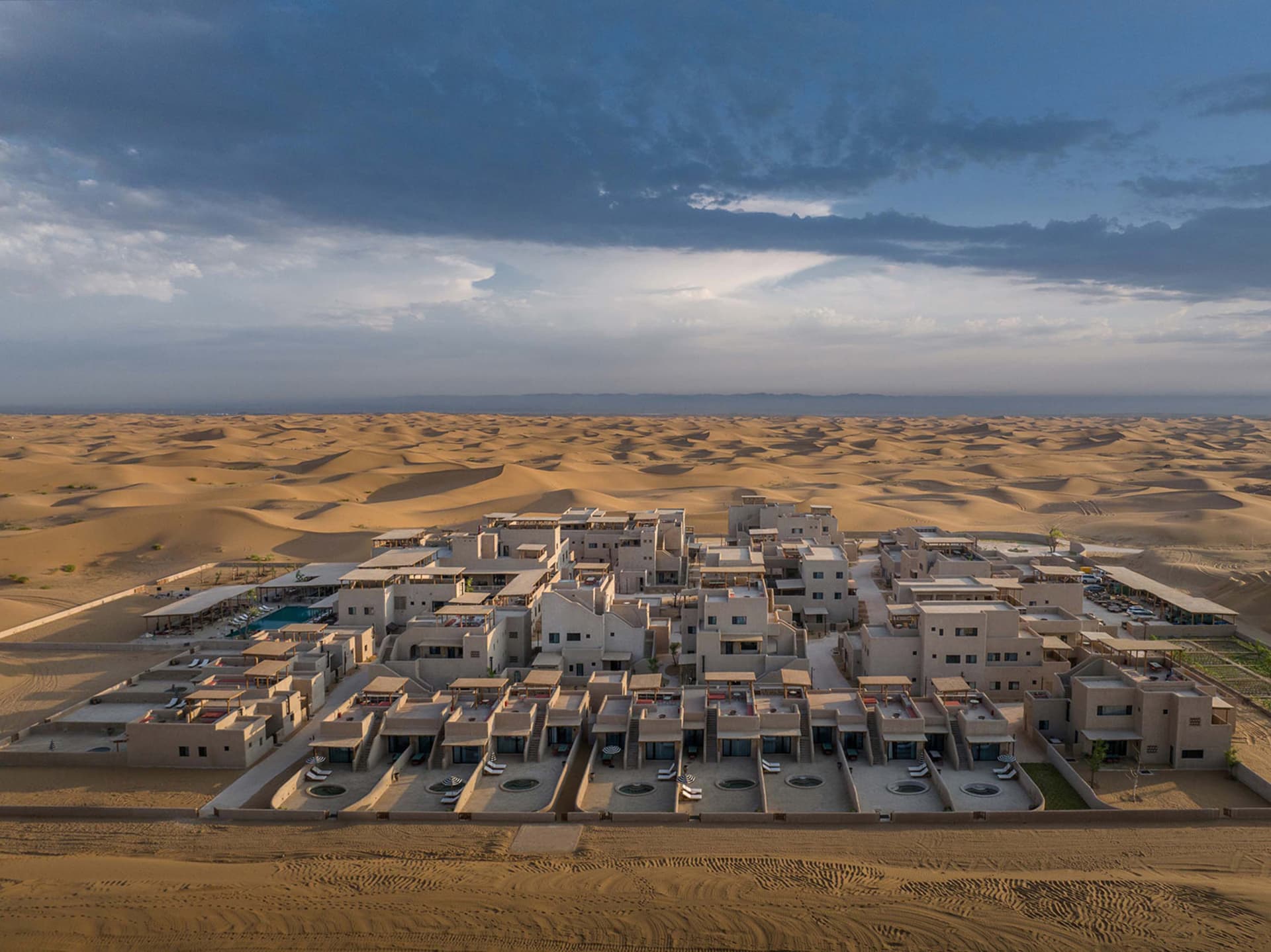 Aerial view of a resort complex in the desert, featuring numerous buildings and structures made of sand.