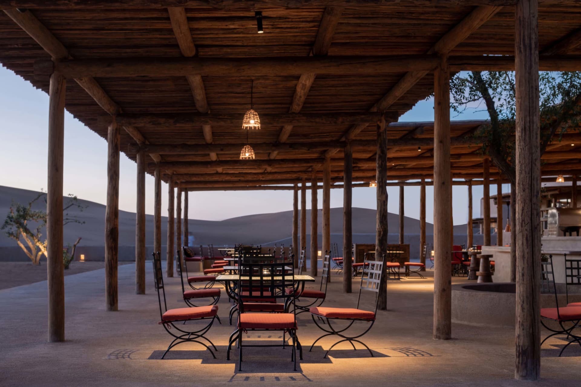 Wooden pergola with tables and chairs under a shaded area in a desert setting