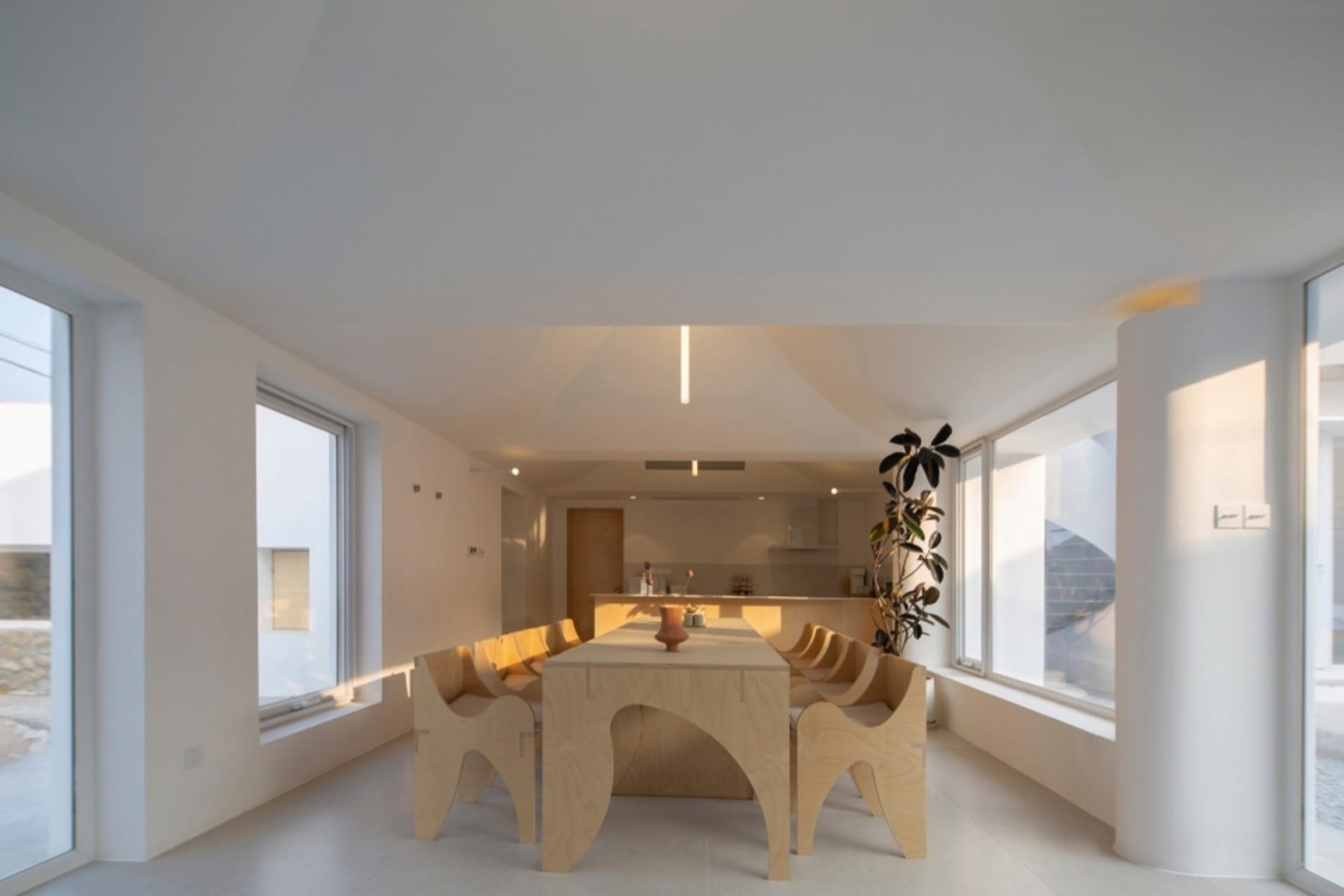 Modern minimalist dining room interior featuring wooden table, chairs, and glass windows, with a potted plant adding life to