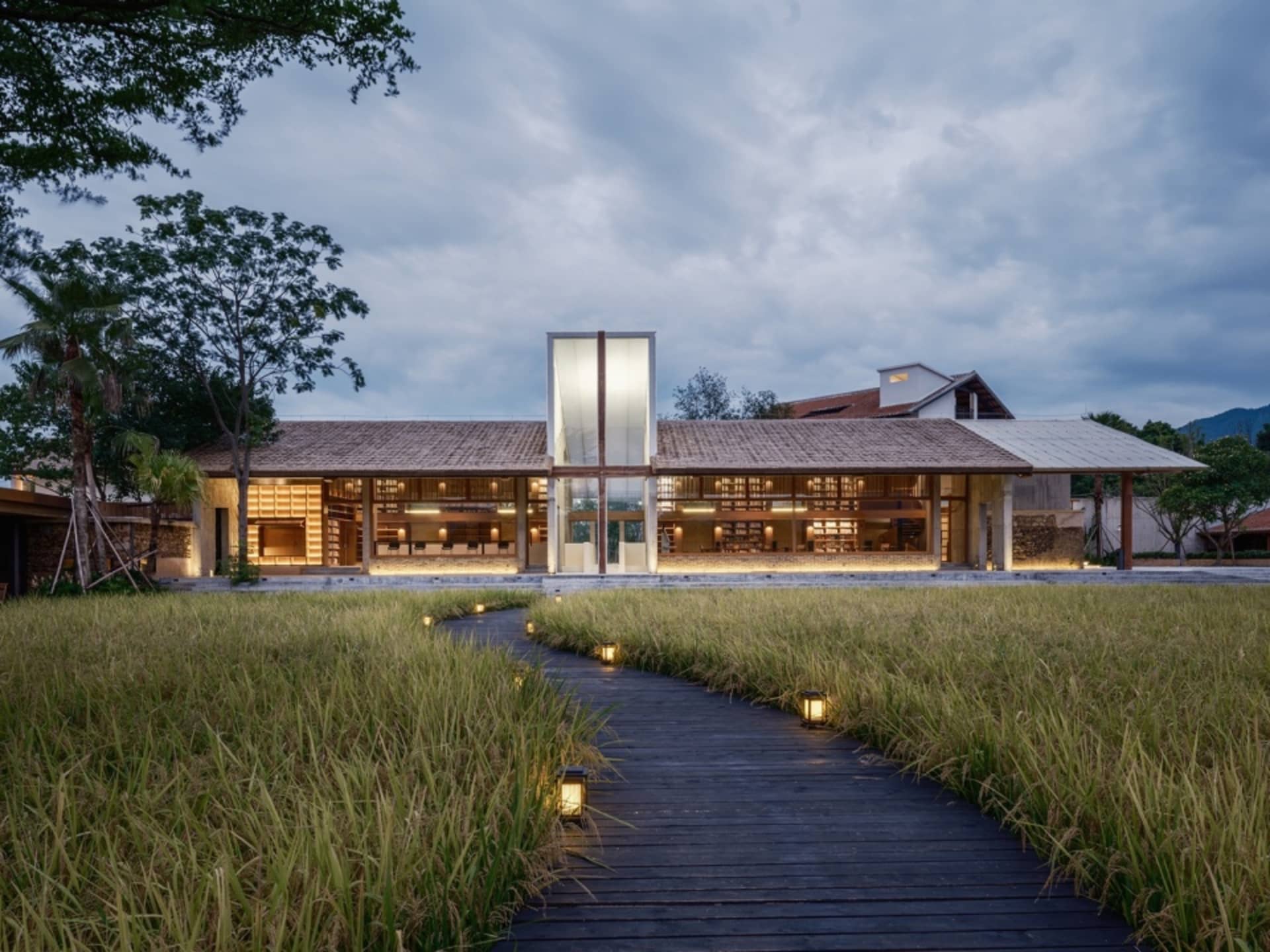 A modern building with wooden exterior and lighting along a pathway surrounded by grass.