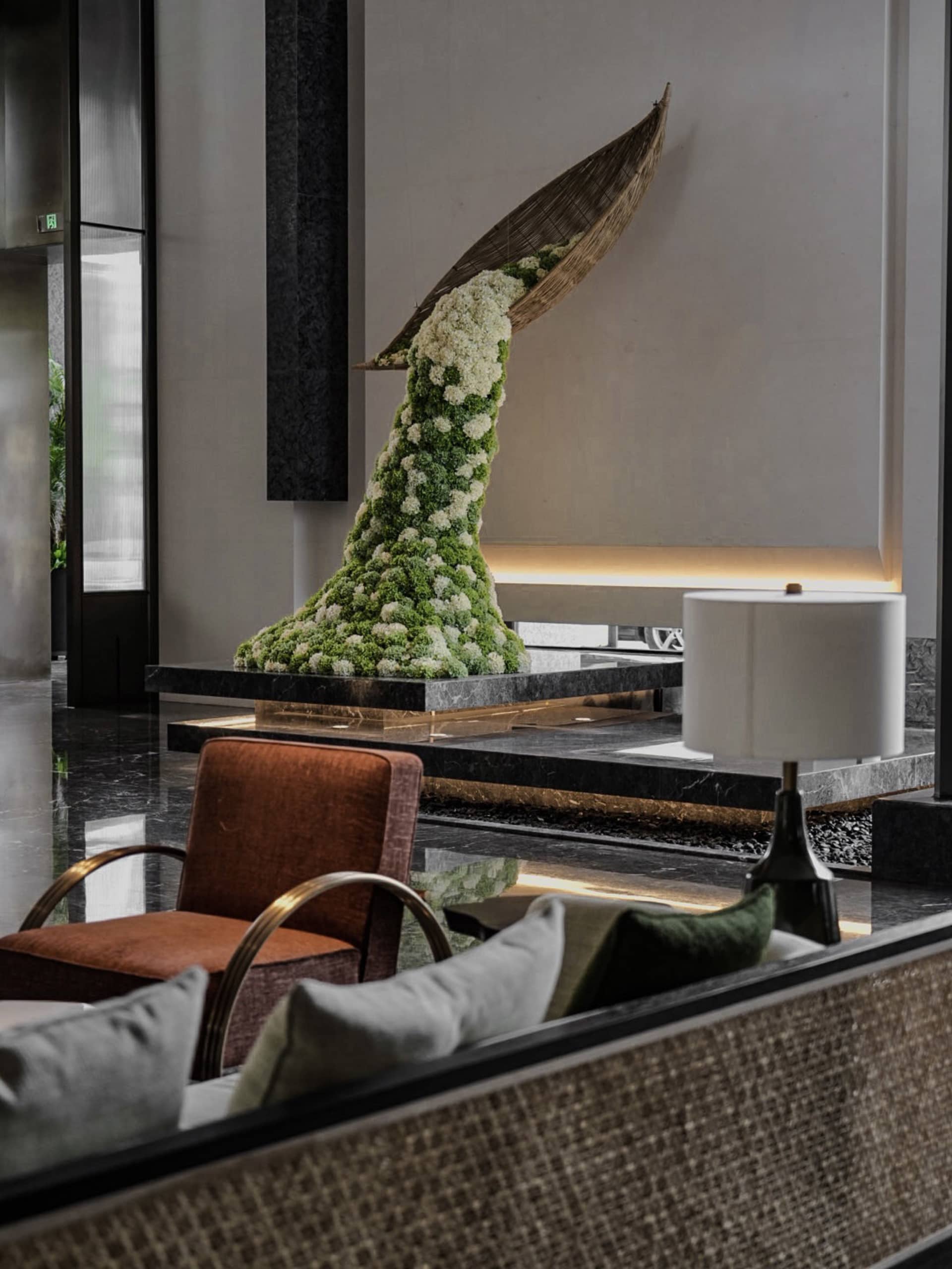 A modern hotel lobby featuring a mixed-materials sculpture on a marble platform.
