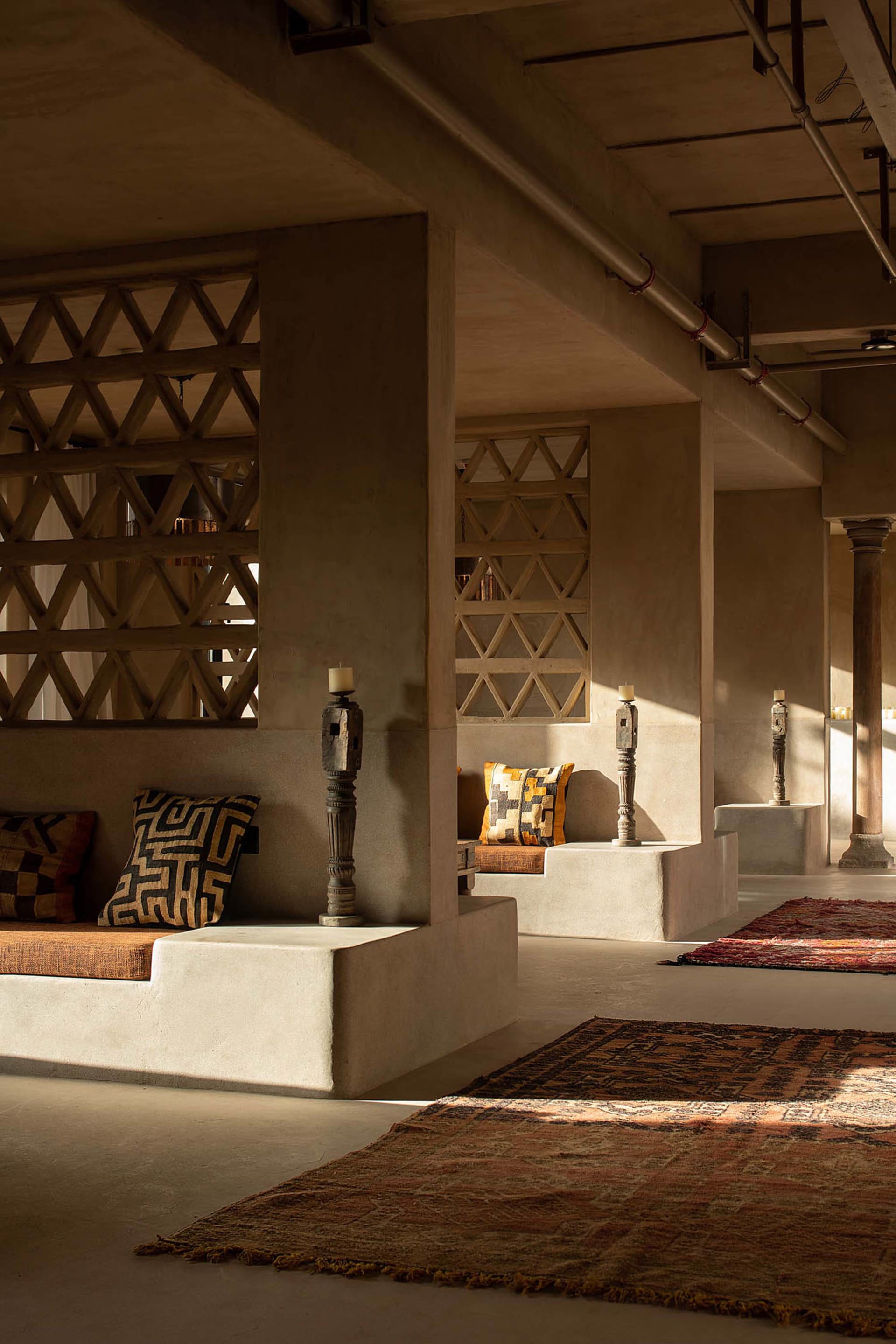 A spacious and modern lobby with concrete seating areas, patterned cushions, and wooden candle holders.