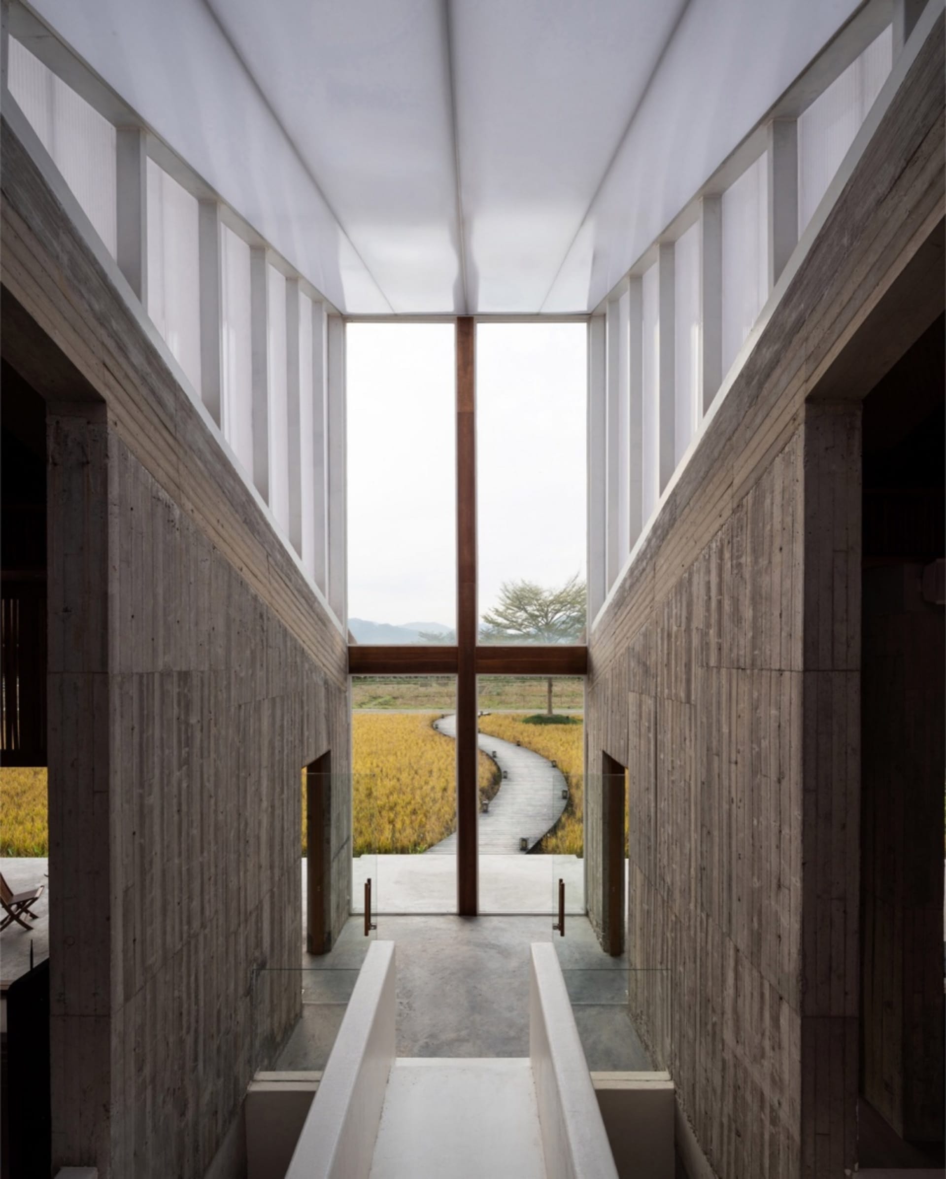Modern lobby with concrete walls, glass windows, and a pathway leading to a natural landscape.
