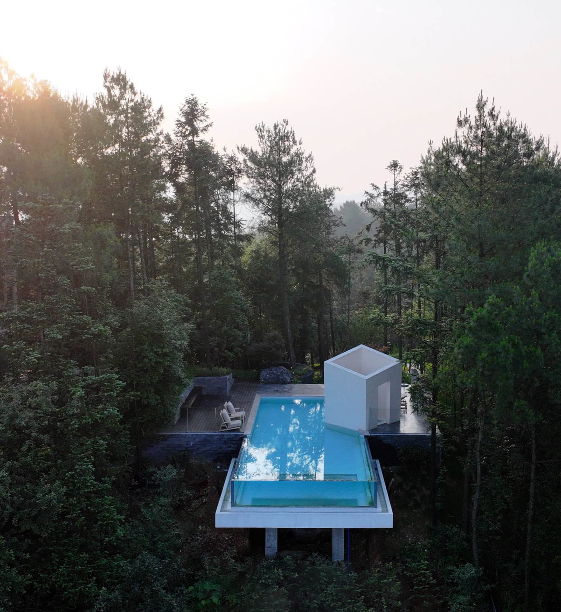 A modern outdoor spa enclosed in glass, surrounded by lush greenery.