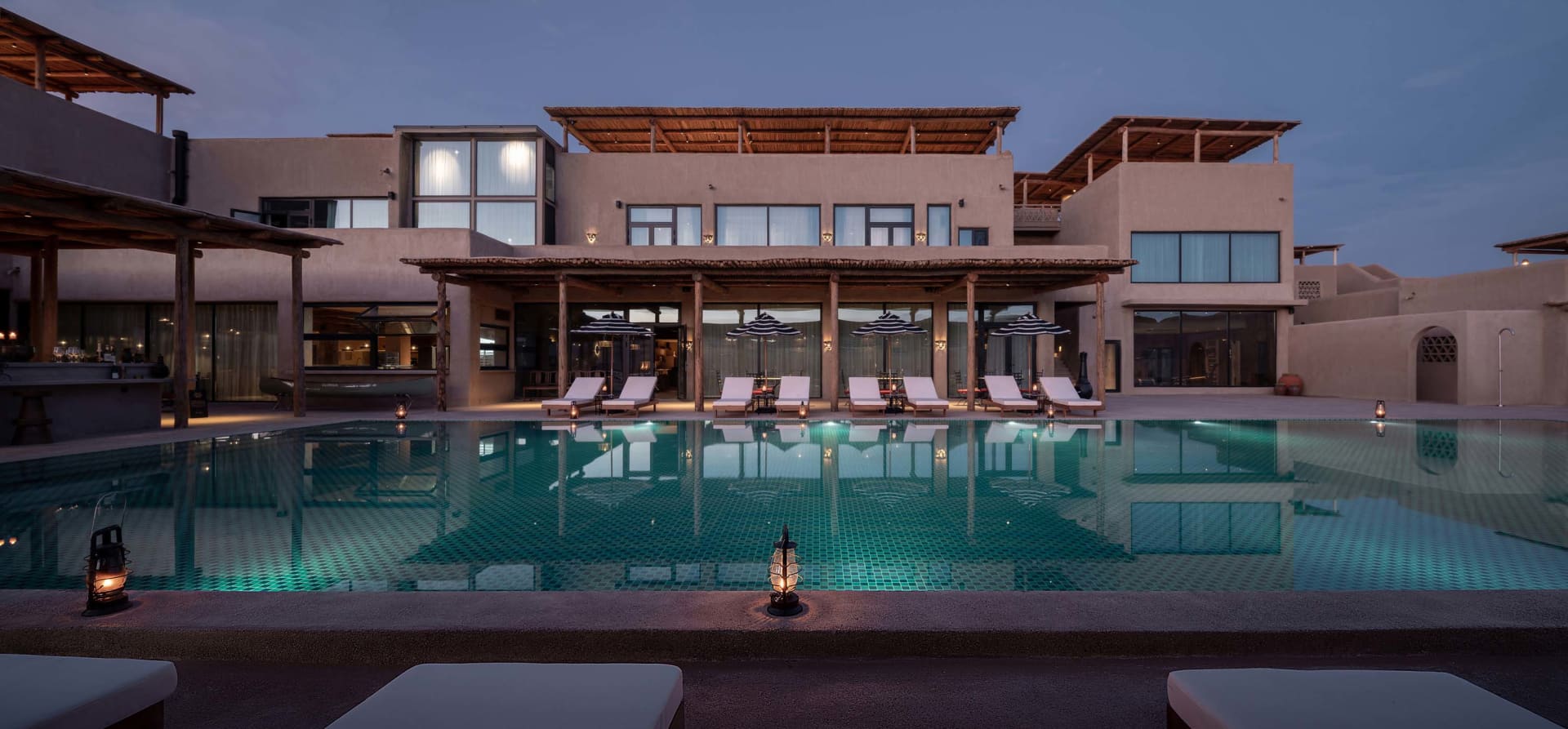 Modern pool house exterior with concrete walls and a serene pool area at dusk.