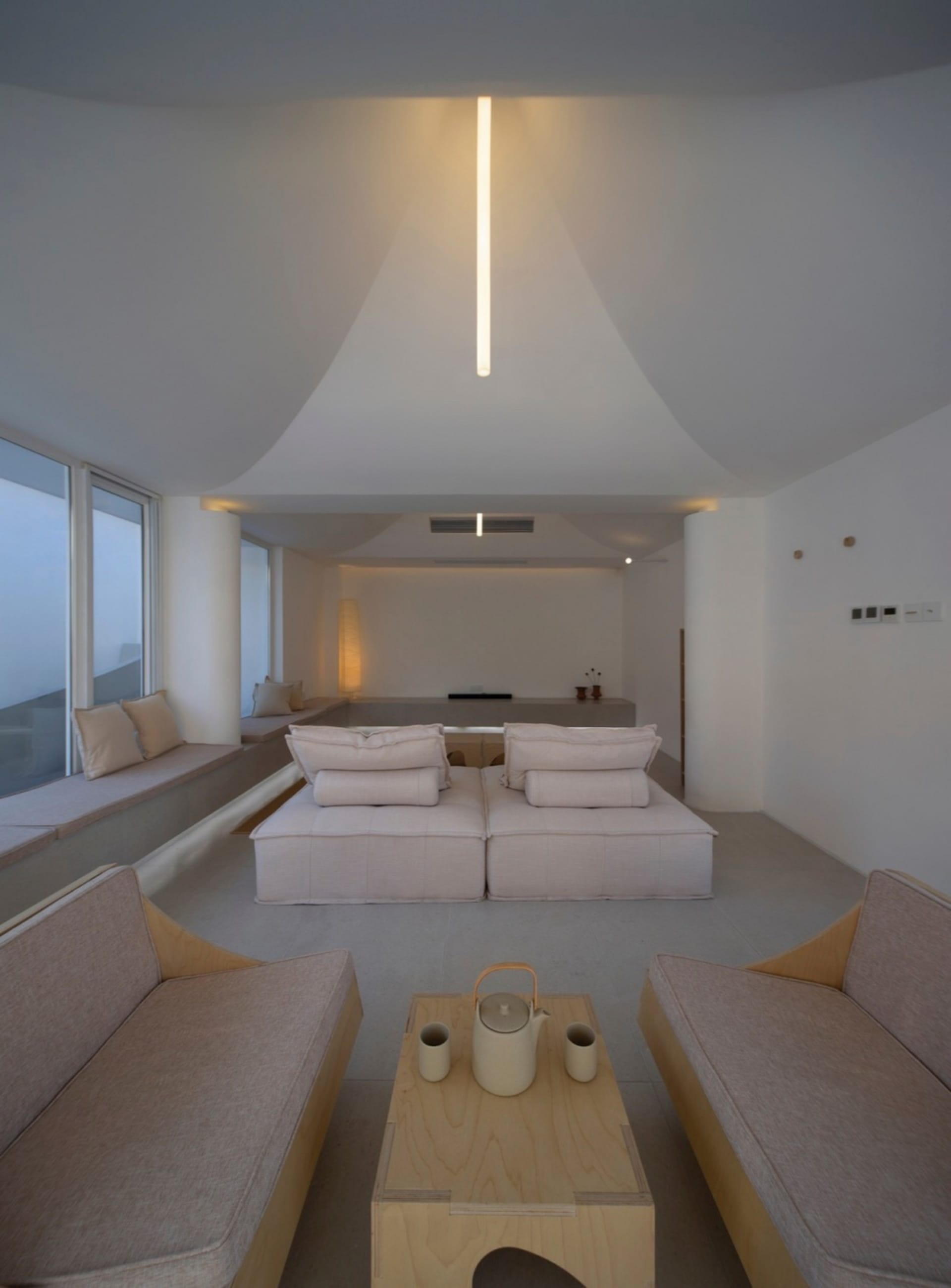 Minimalist living room with concrete walls, floor, and furniture. Light wooden coffee table with teapot and cups.