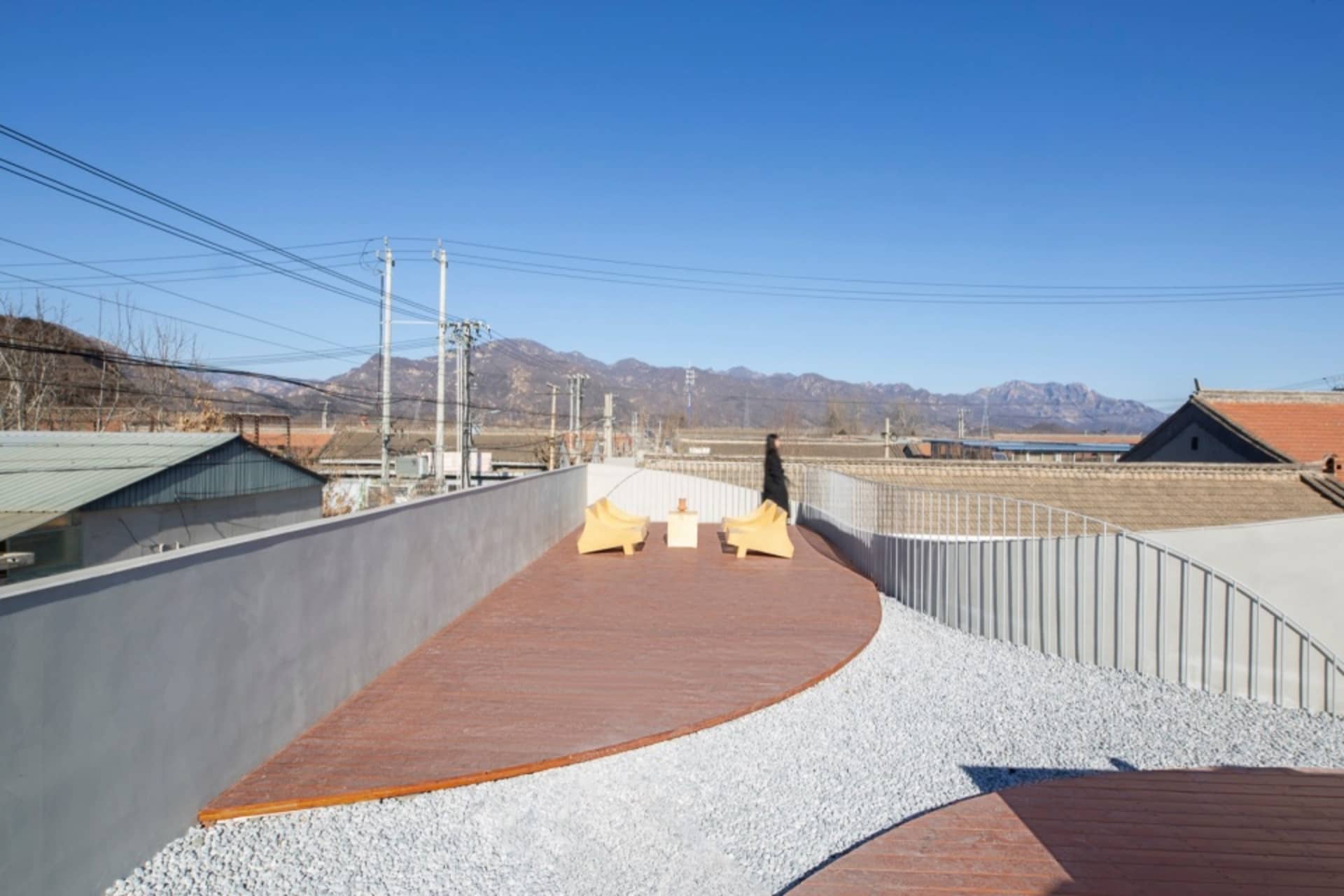 A minimalist roof deck featuring wood planks, with a person walking in the background.