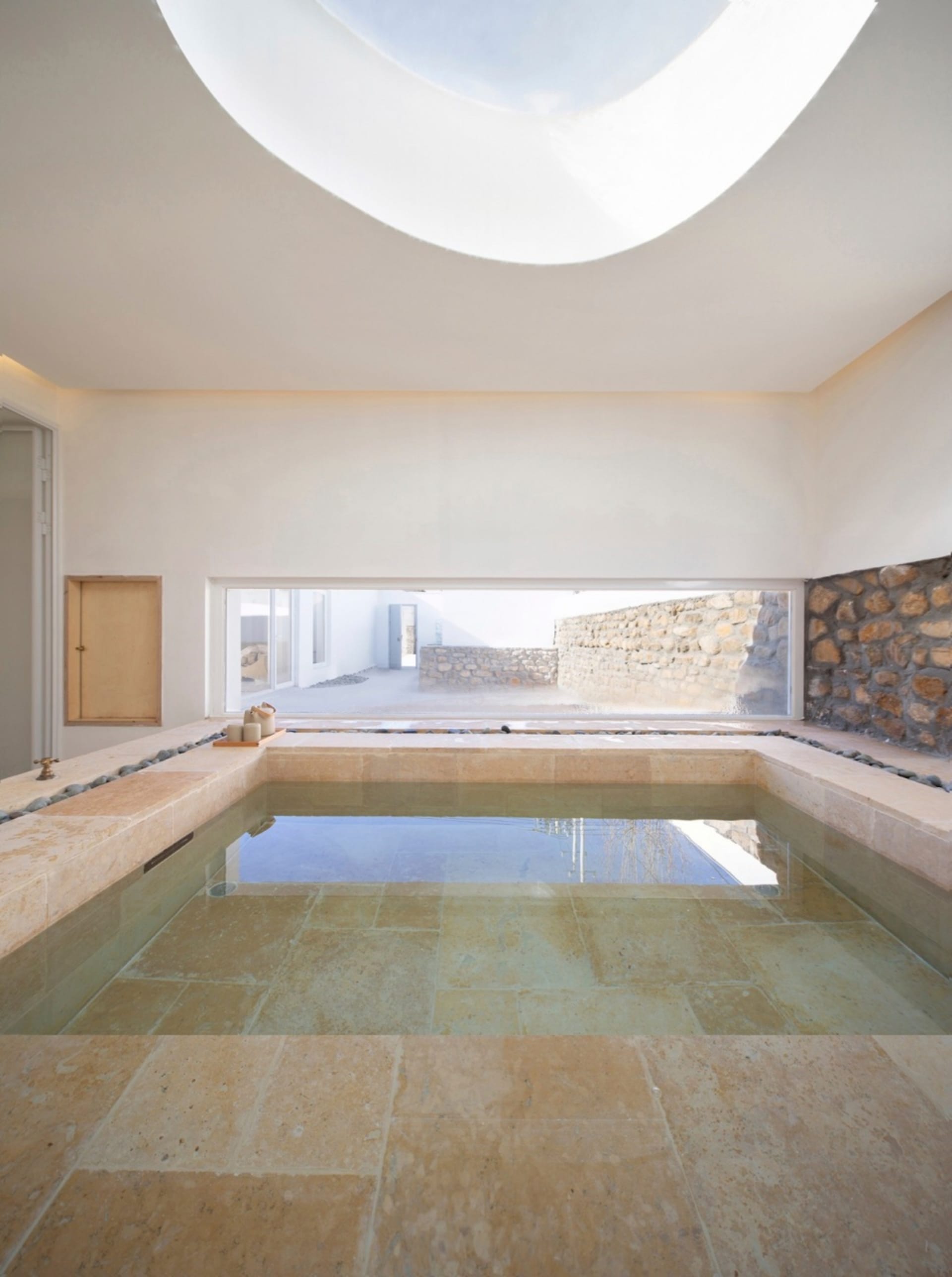 A minimalist indoor swimming pool with stone tiles and a skylight.