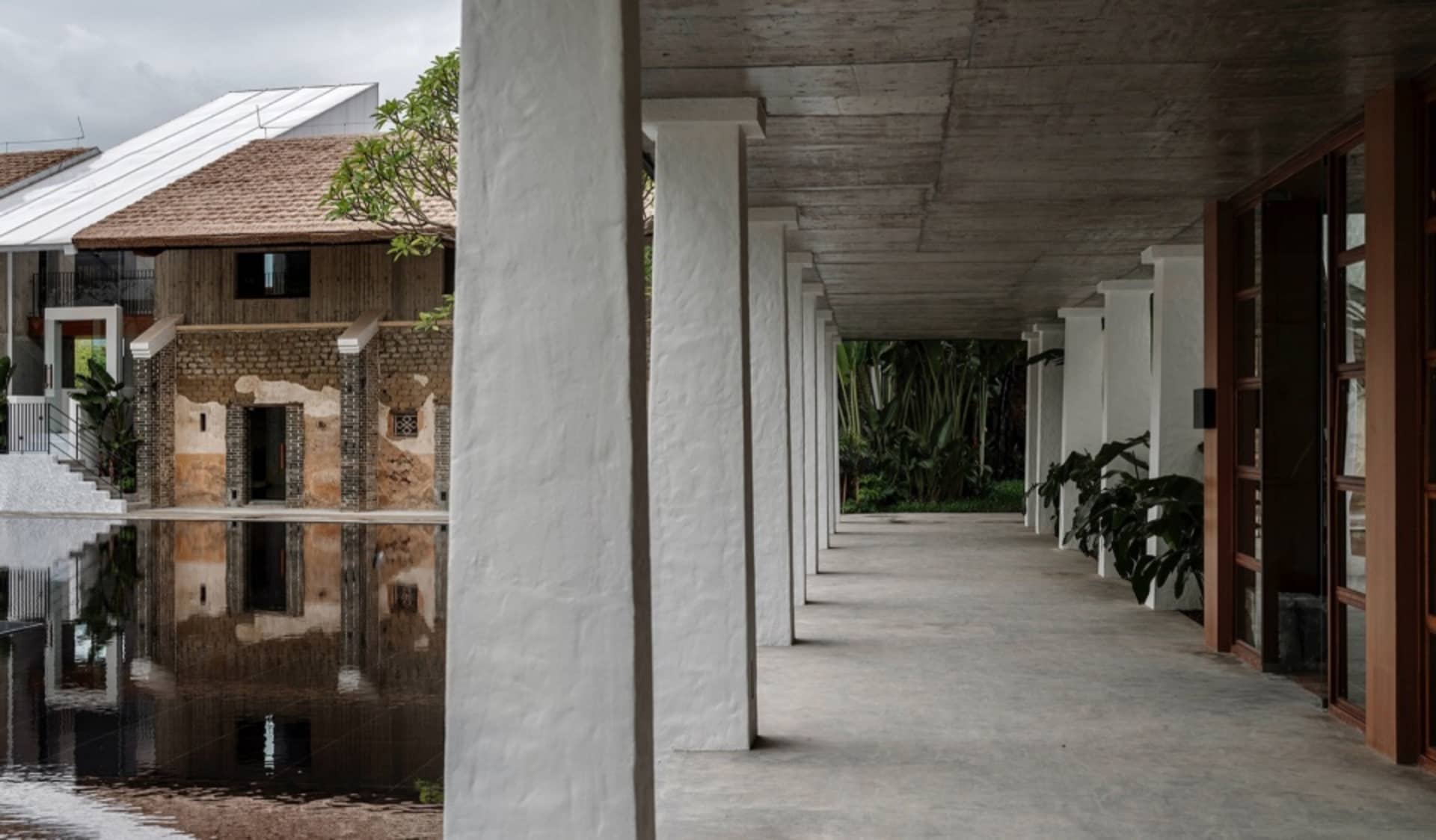 A modern residential space featuring a concrete porch with greenery and water reflection.