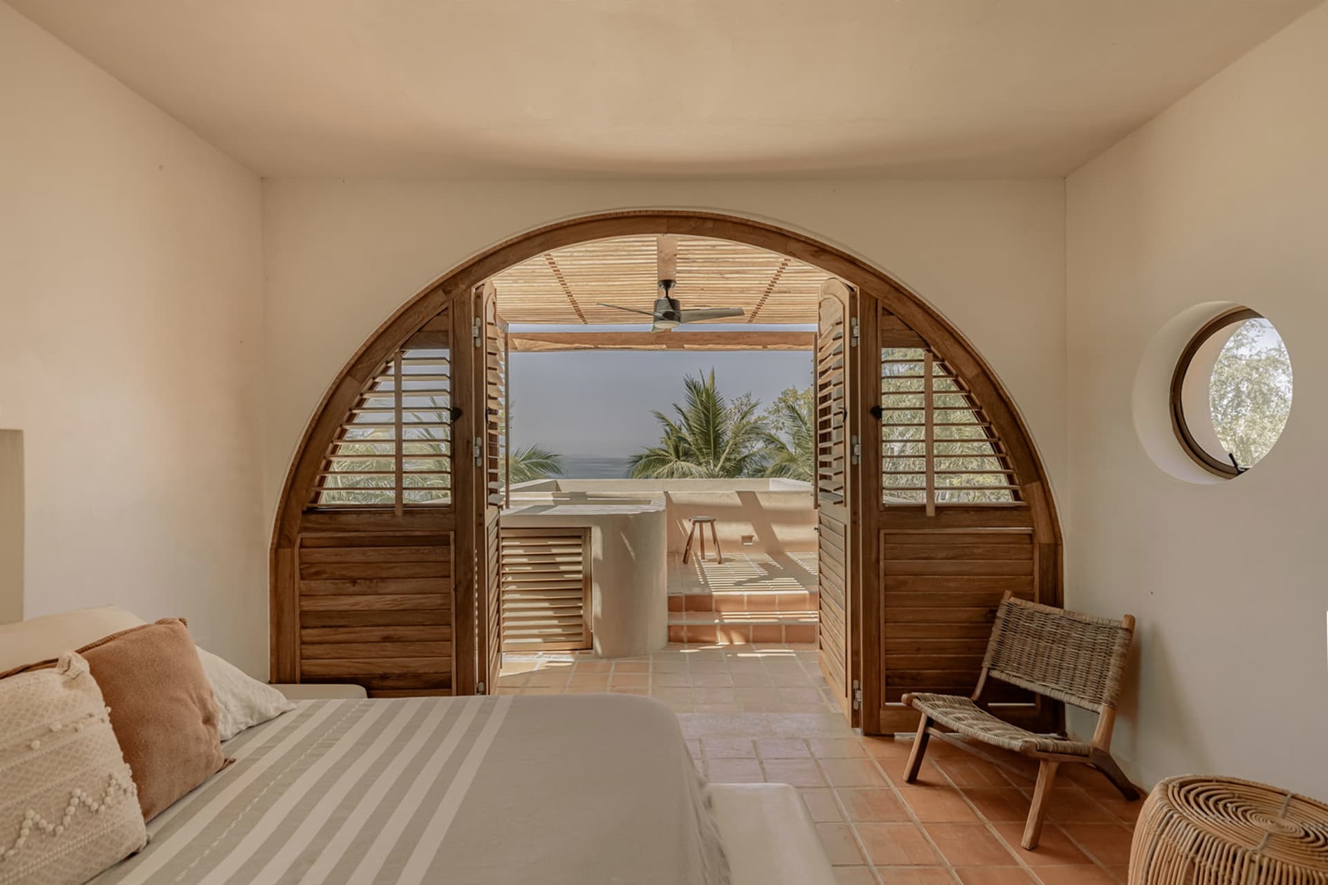 Bedroom with wooden doors and tile floor, featuring a bed with striped bedding and a wicker chair
