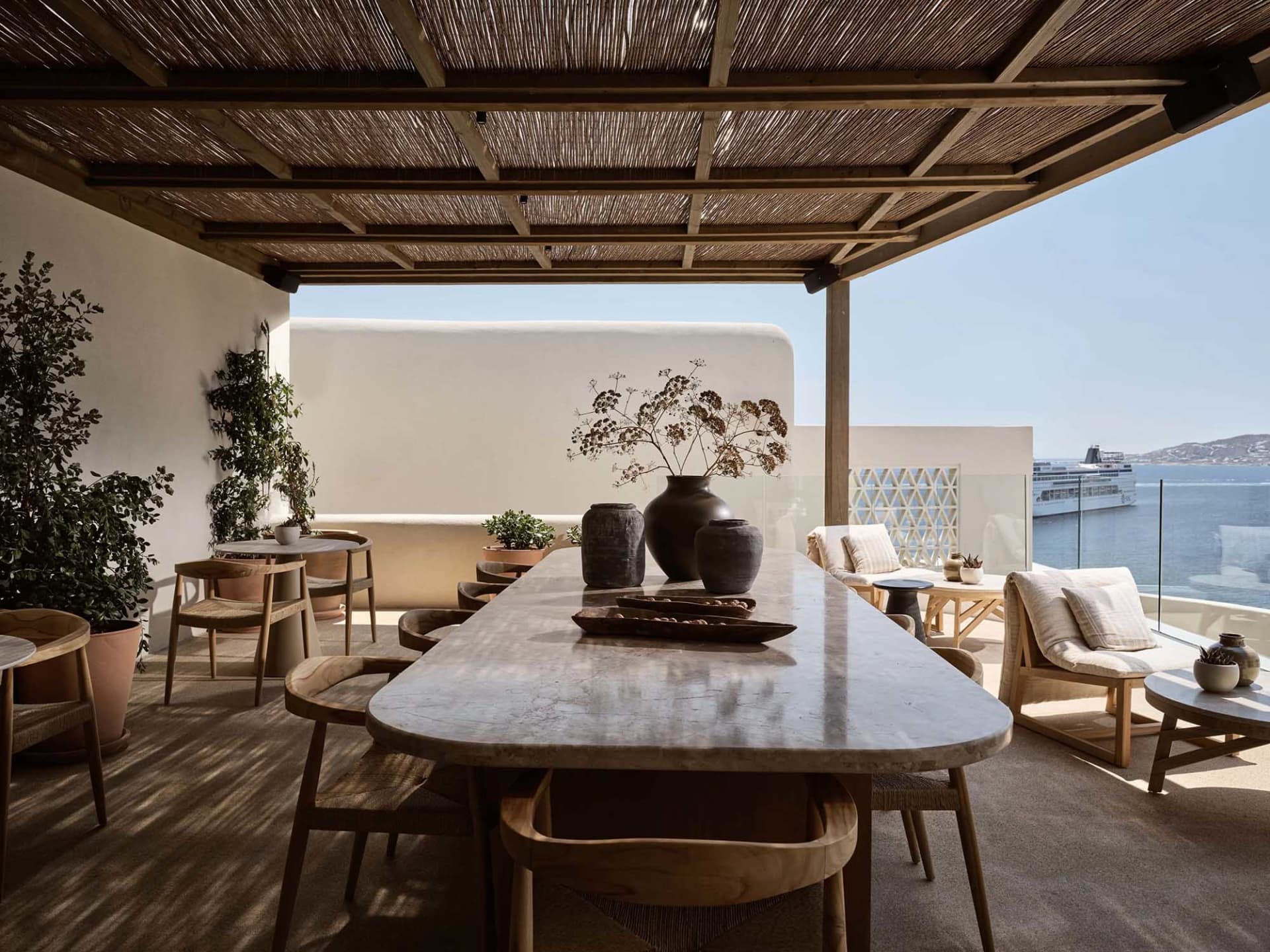 A minimalistic outdoor patio with wooden furniture and stone table, overlooking the ocean and a cruise ship.