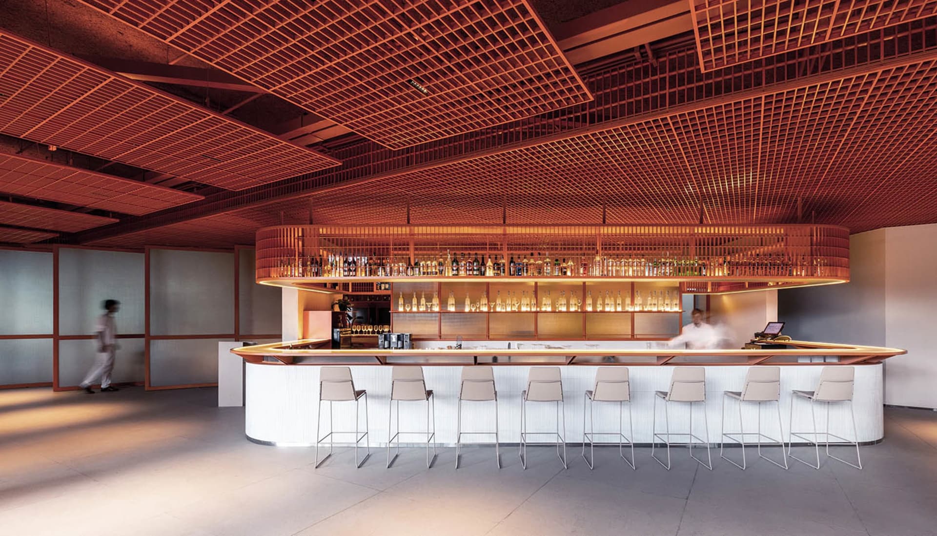 A minimalist bar counter with metal stools and a metal ceiling grid