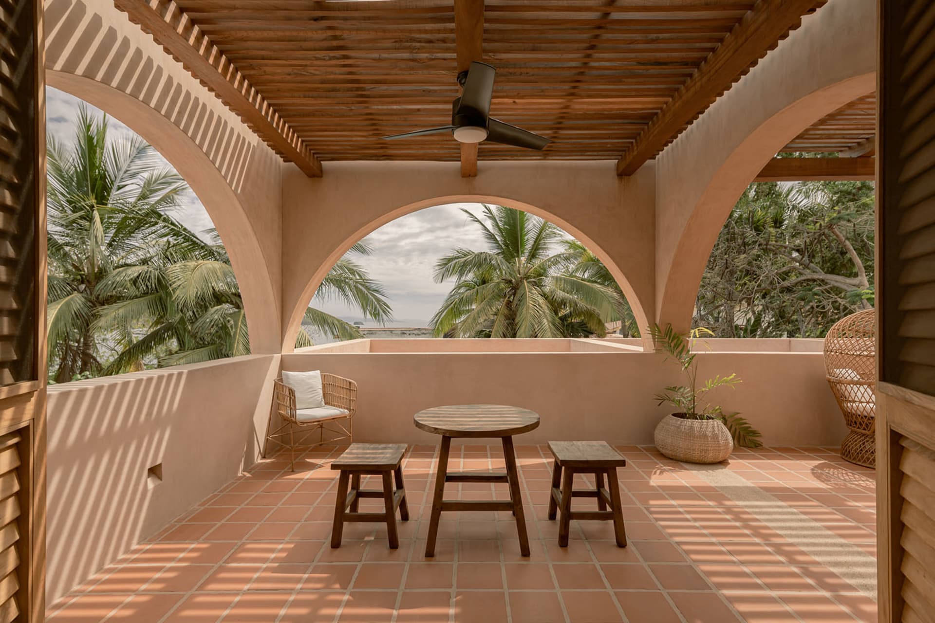 Vacation home veranda with wooden pergola, terracotta tiles, and tropical foliage.
