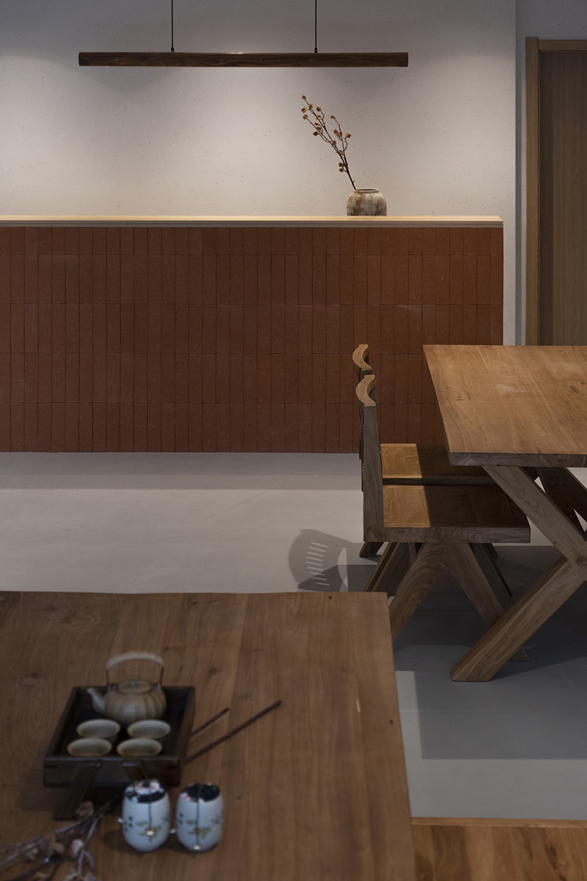 A minimalist dining room featuring wooden furniture and a wooden table with tea set and chopsticks.