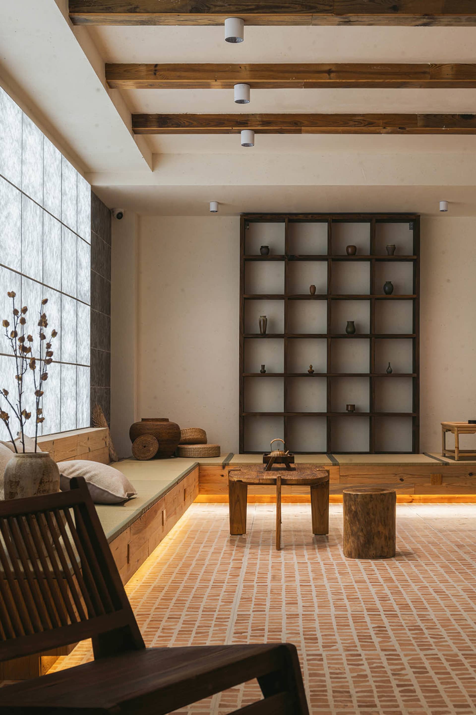 A modern living room with a wooden floor, low wooden furniture, and a large window.