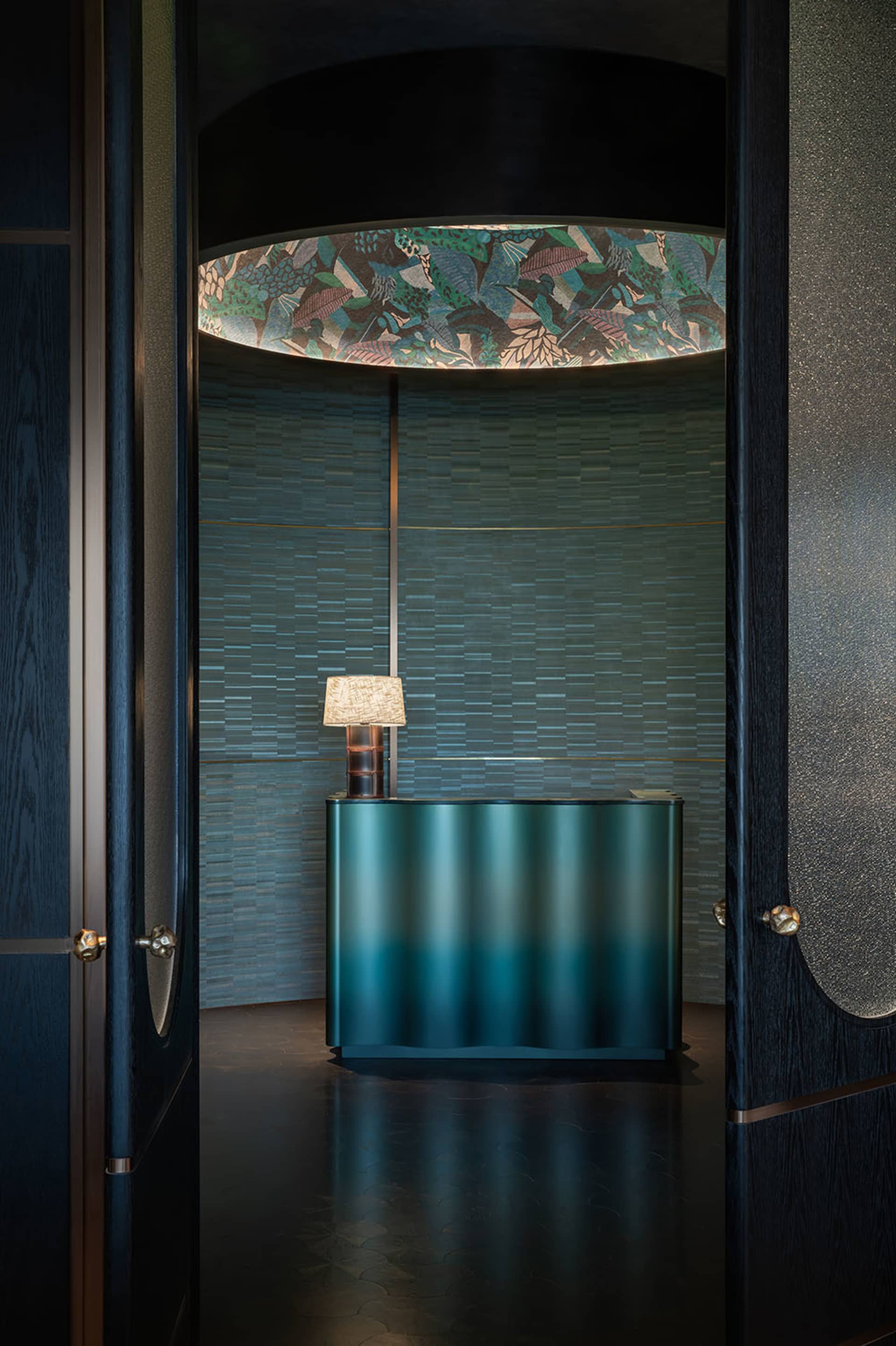 Modern reception desk with metallic finish, featuring a lamp and a patterned ceiling light.