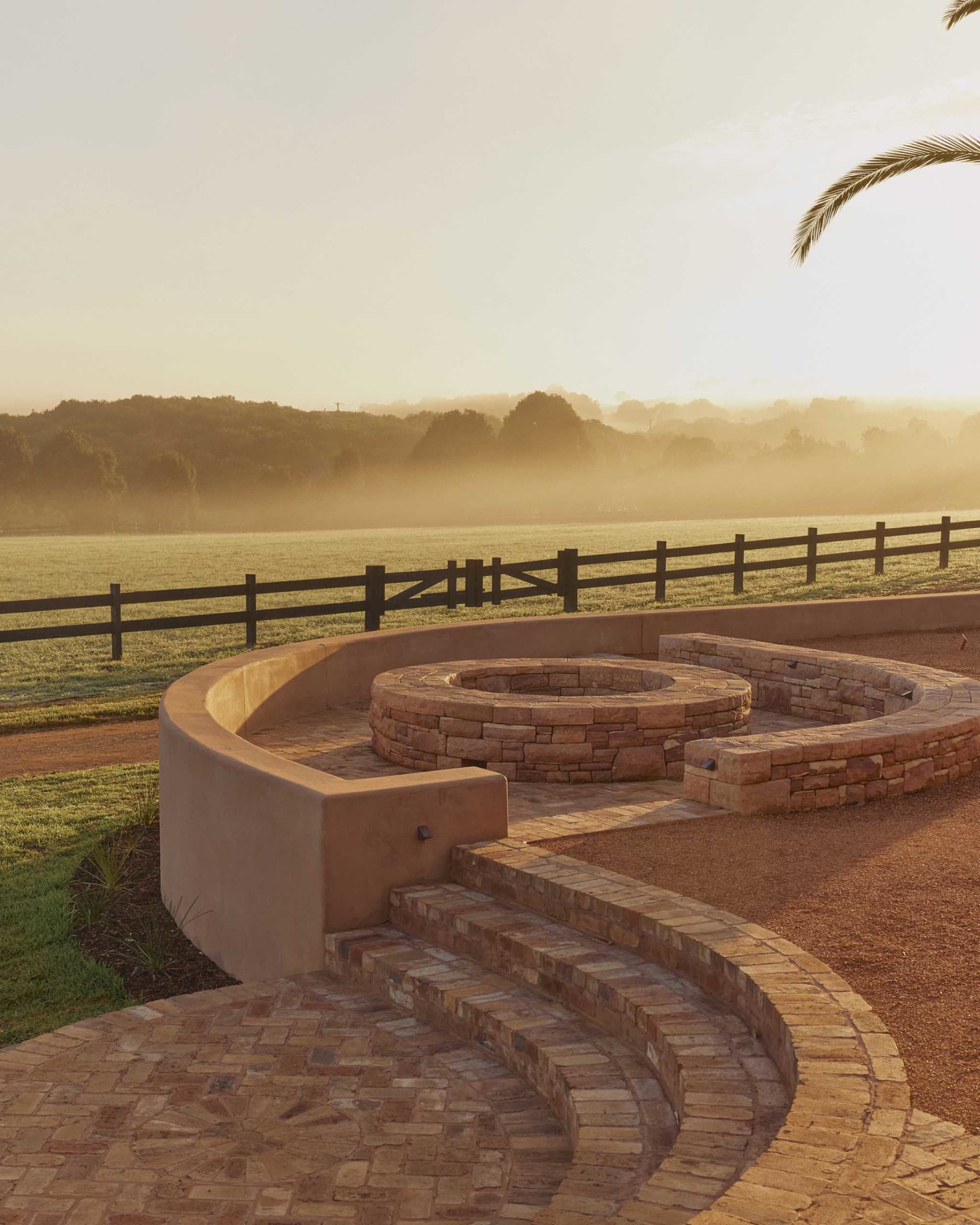 A landscape featuring a brick stone fire pit surrounded by a circular seating area.