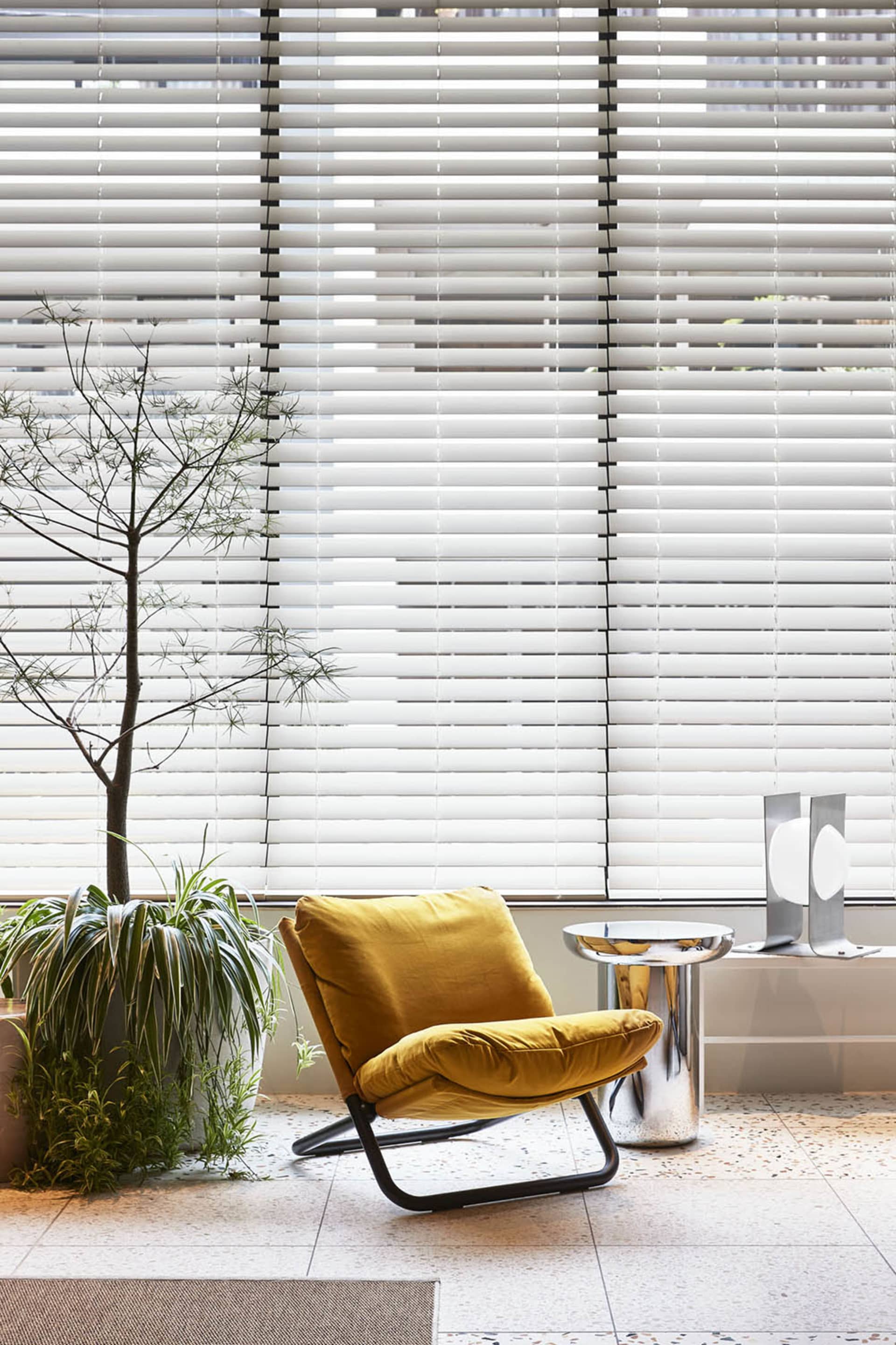 A modern living room featuring a yellow velvet chair with metallic legs, a sleek metallic side table, and a plant.