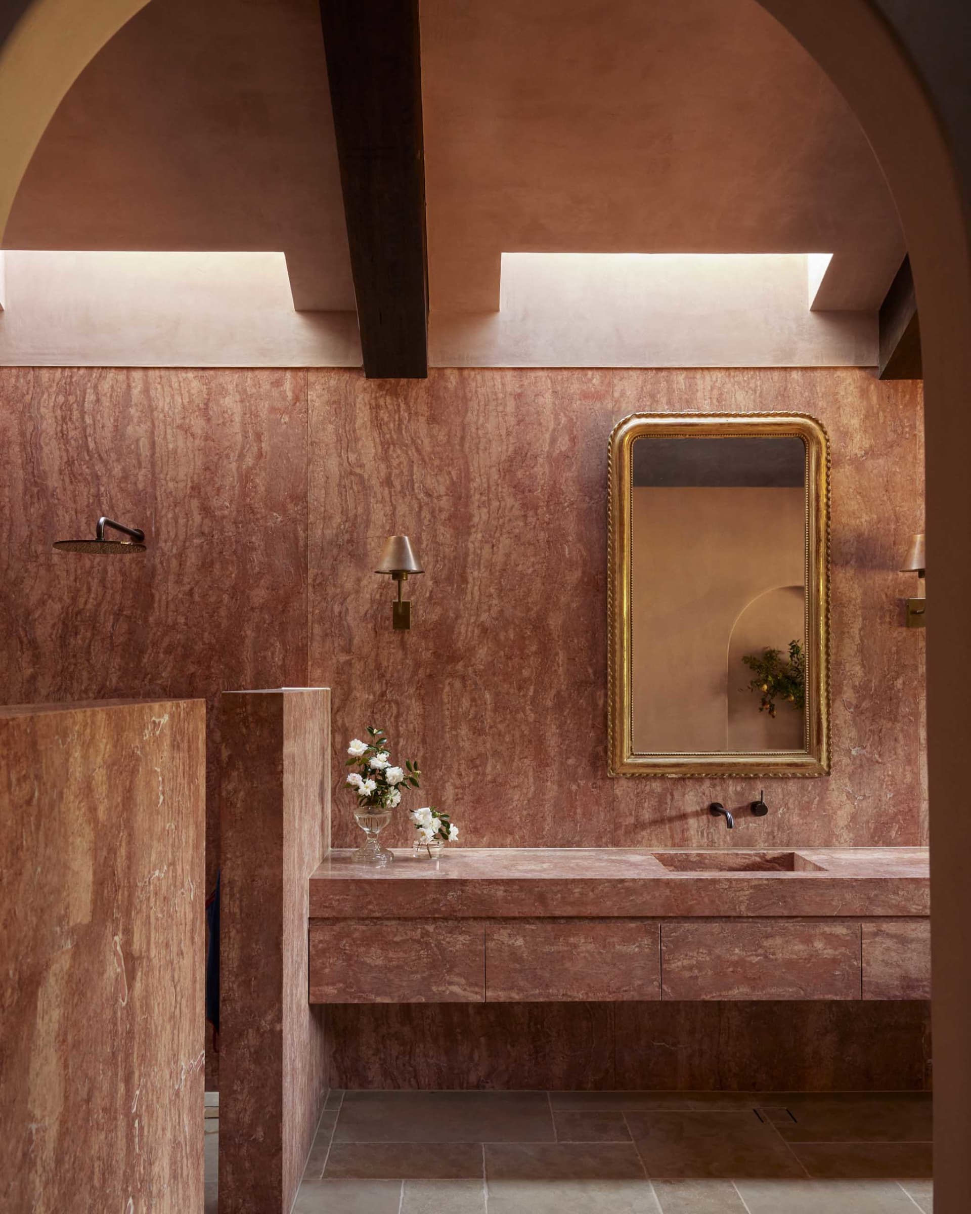 A modern bathroom featuring marble walls and a floating vanity with a golden-framed mirror and sleek fixtures.