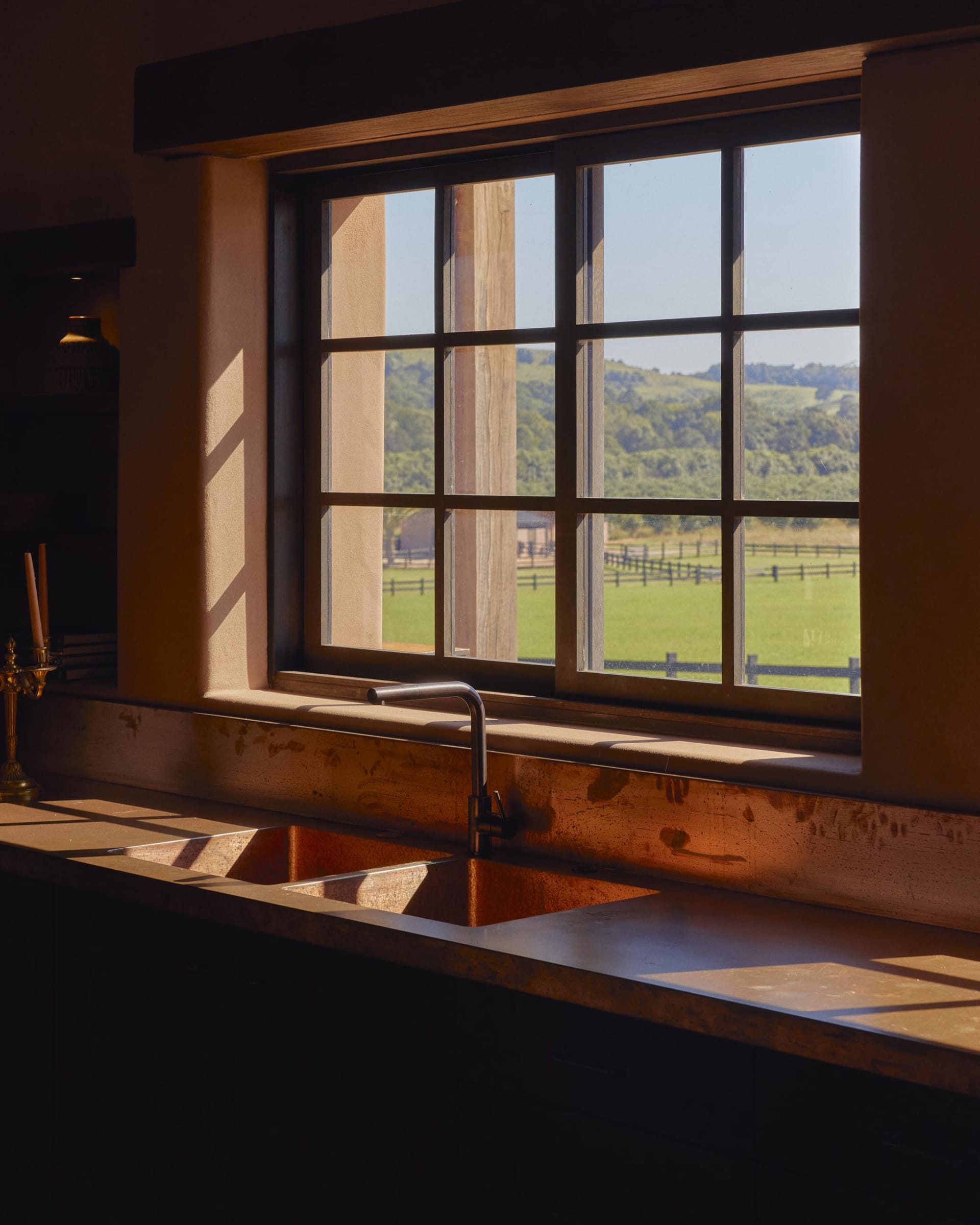 Modern kitchen scene featuring a copper sink with backlit countertop, overlooking a lush green landscape with a wooden frame