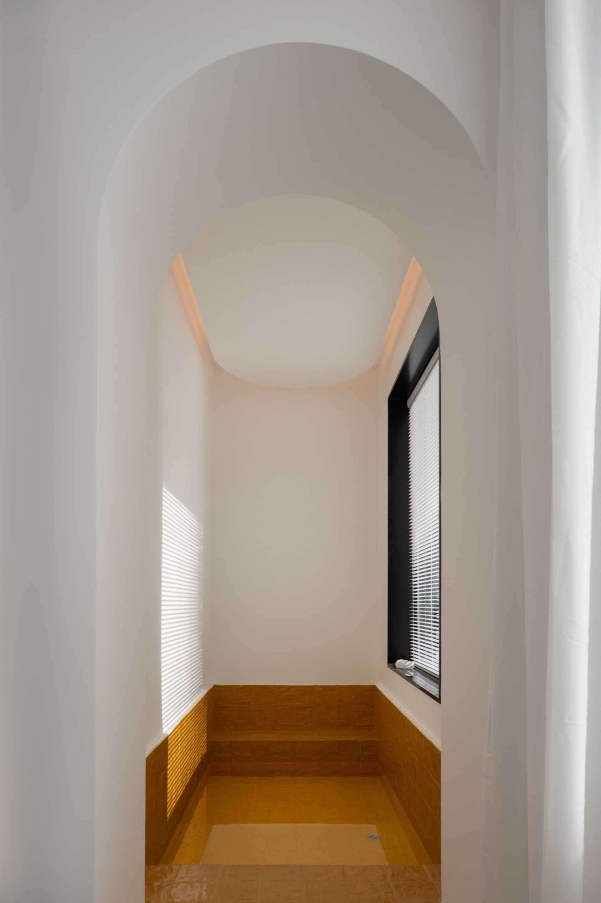 A minimalist bathroom with white tiled walls and floor, featuring a walk-in shower.