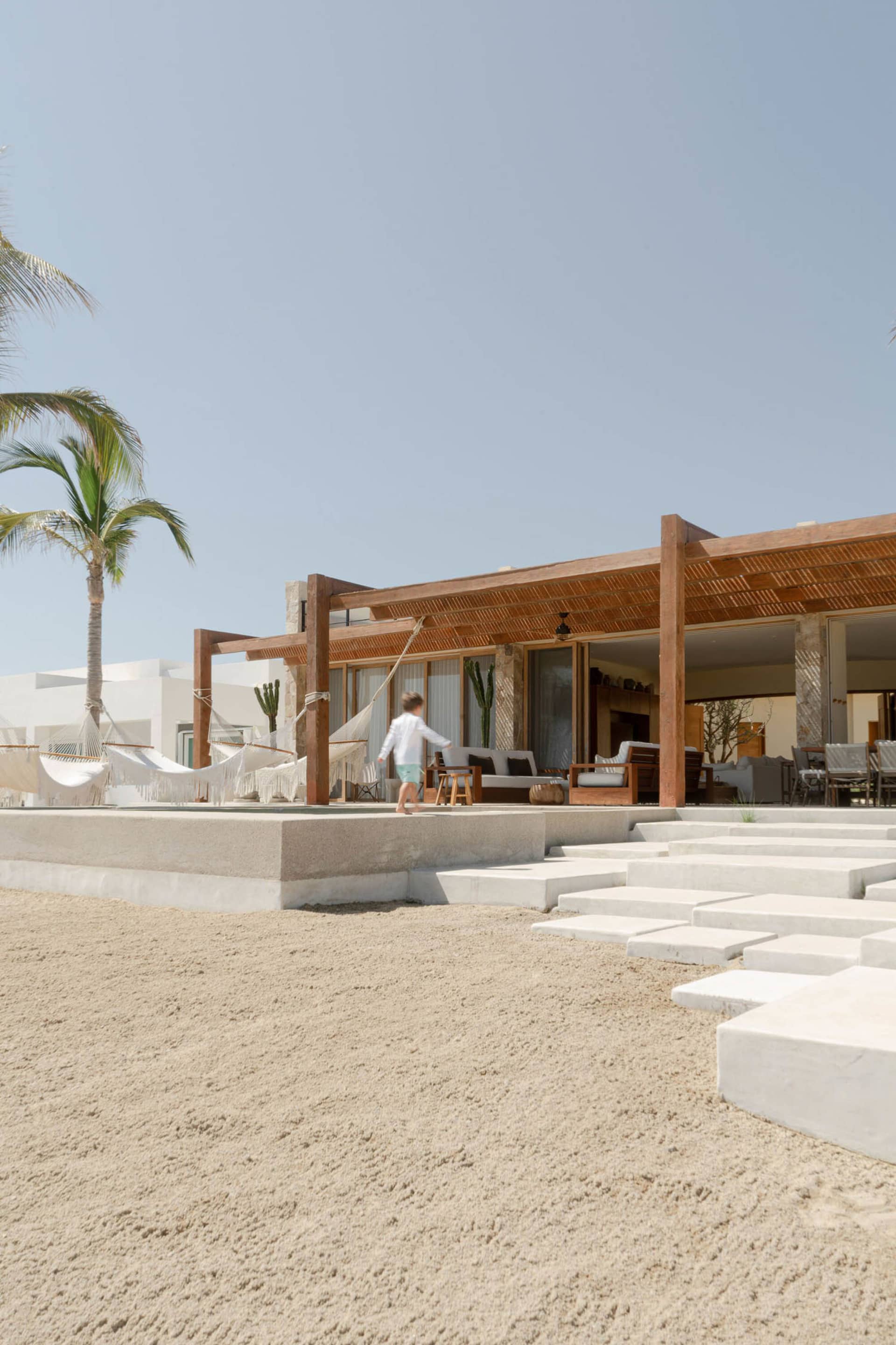 A beachfront resort with concrete and wooden structures, featuring a walkway and outdoor seating.