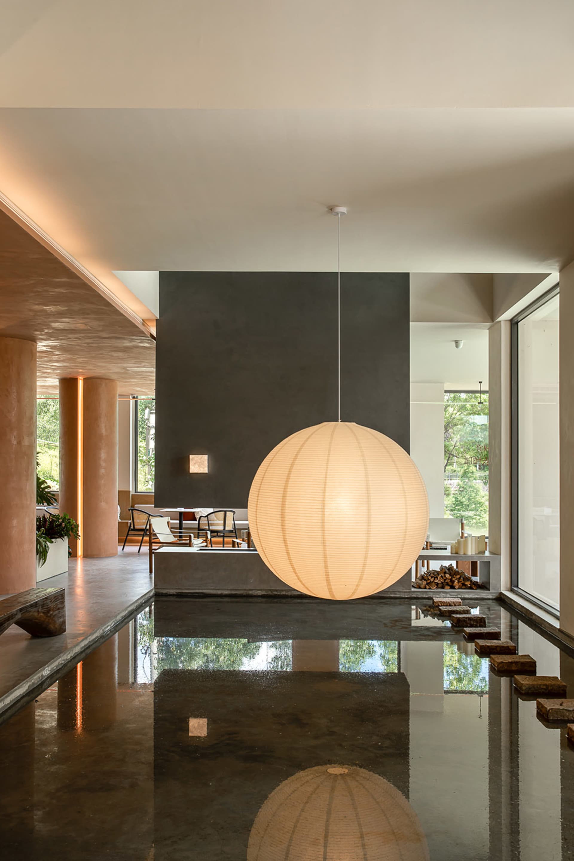 Modern minimalist living room with concrete walls and a large spherical light fixture hanging from the ceiling.