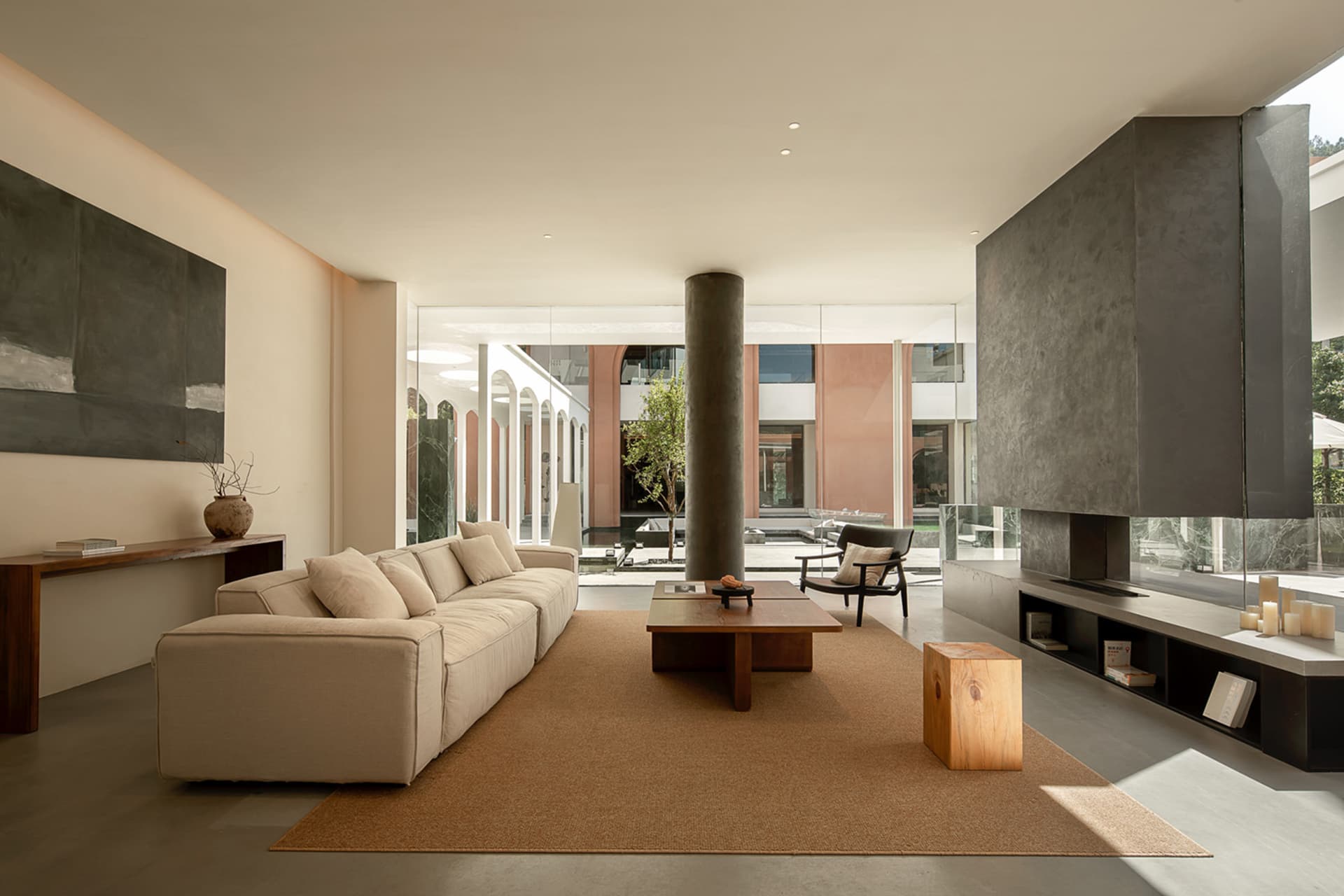 A minimalist living room with concrete walls, floor, and furniture, featuring a large beige sofa, a wooden coffee table, and