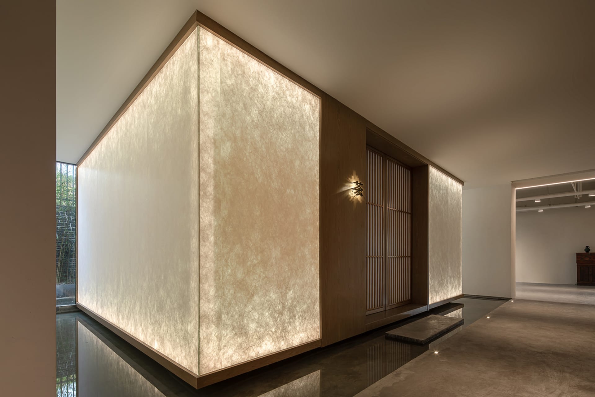 A minimalist lobby with paper walls and wooden partitions illuminated by warm lighting.