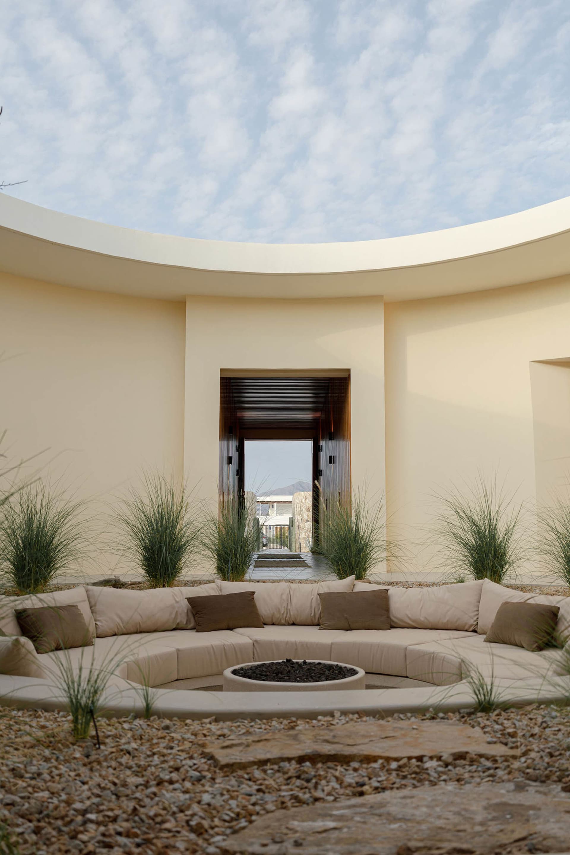A modern architectural exterior featuring a circular, concrete space with seating and a fire pit.