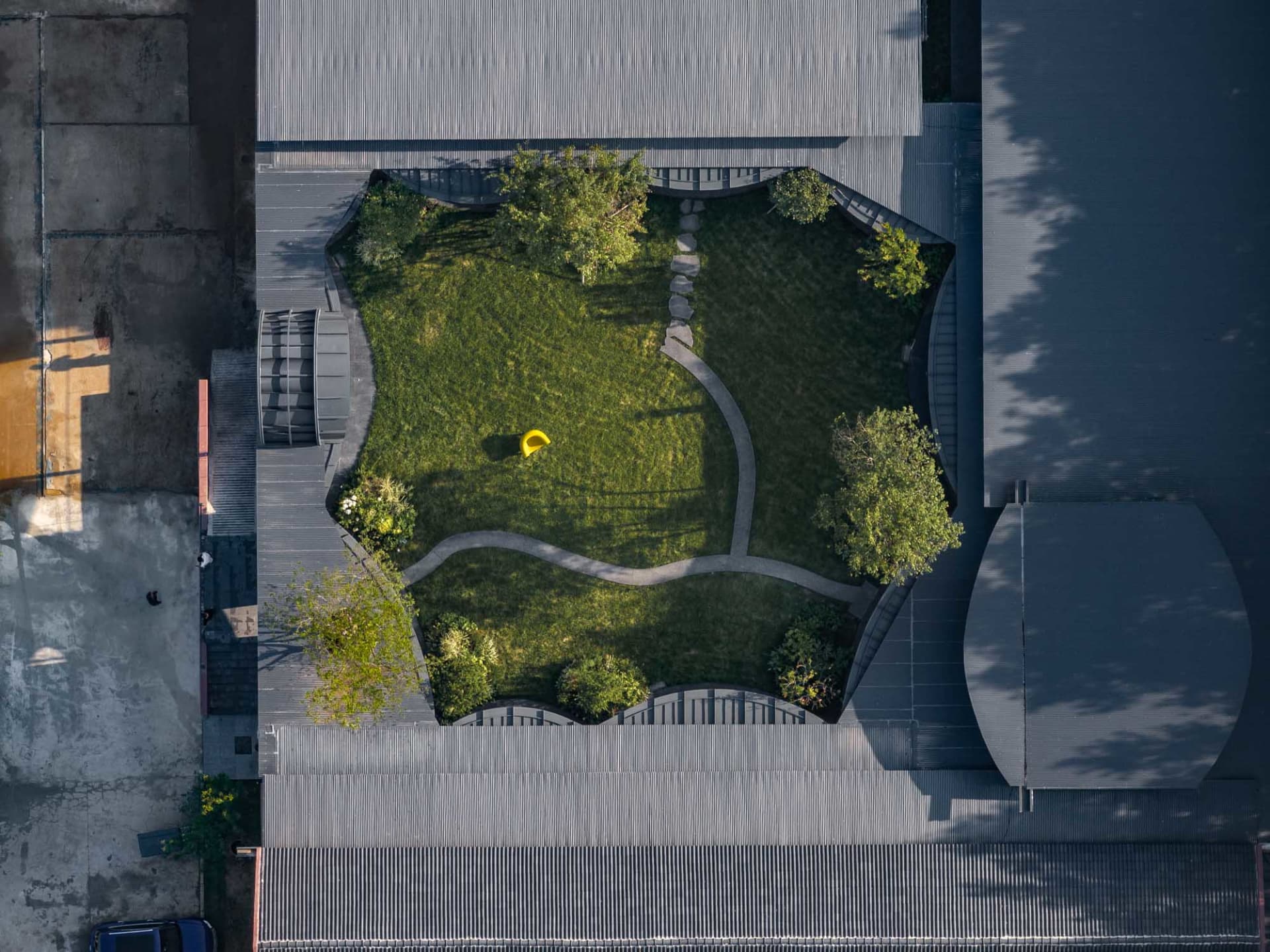 A modern, green garden with a yellow sculpture and a curved path surrounded by buildings.