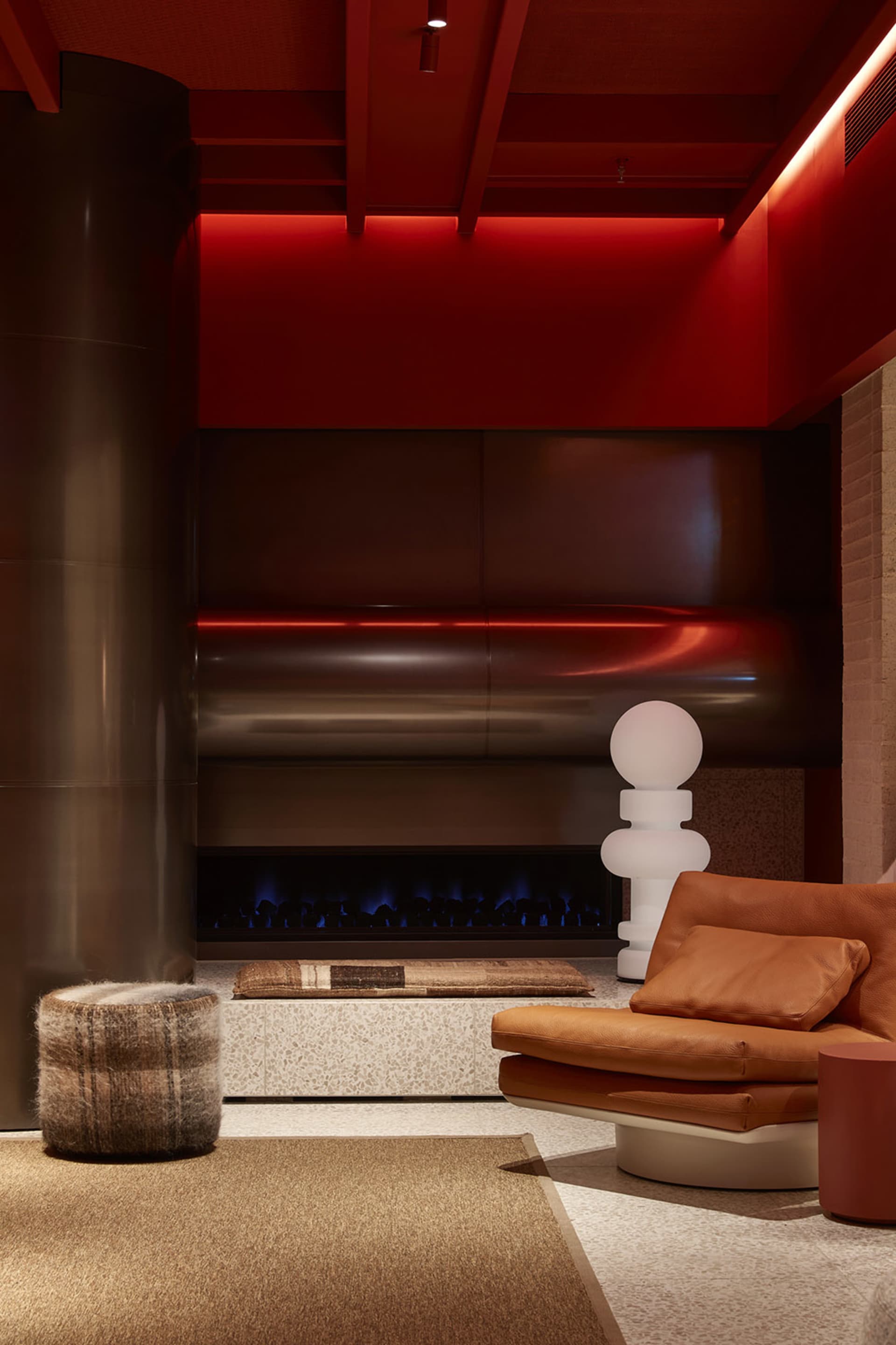 A modern living room with concrete walls, a leather sofa, and a fireplace with red lighting.