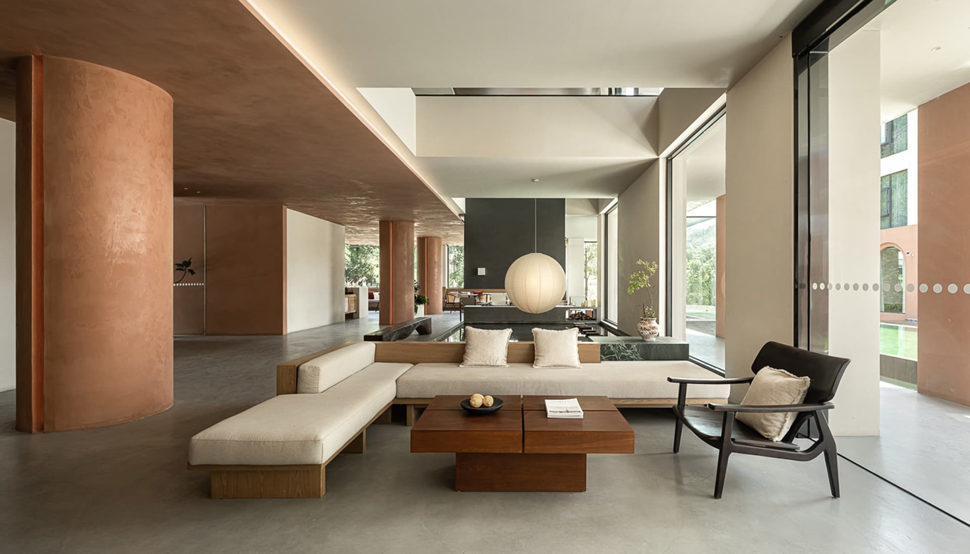 A modern minimalist living room featuring a concrete floor, wood furniture, and a minimalist pendant light.