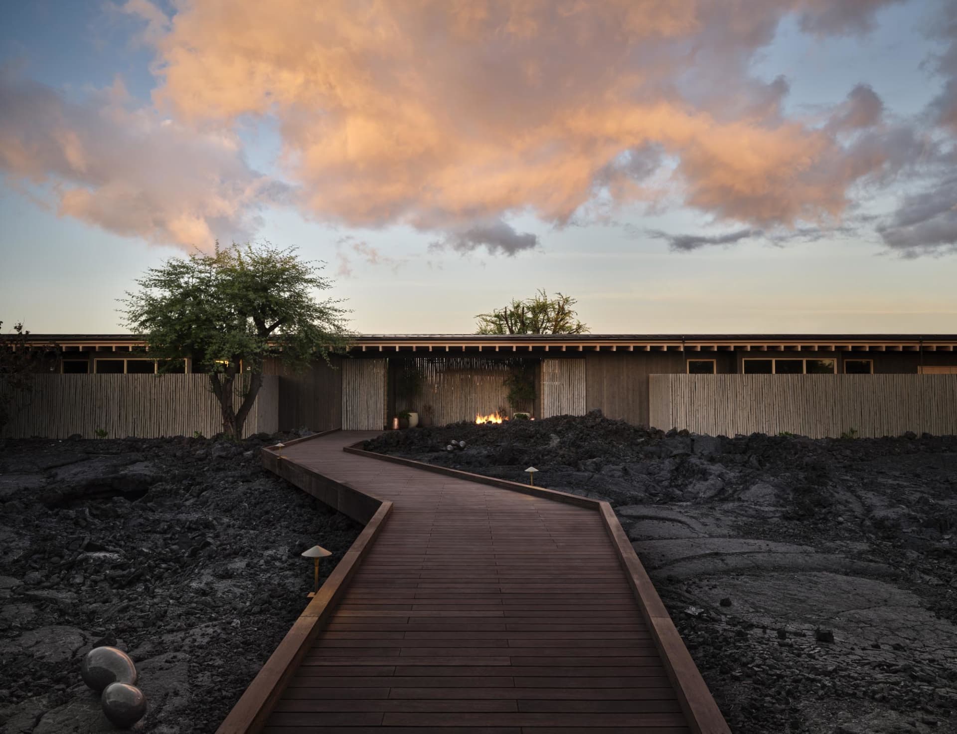 A modern residential spa setting with a wooden and bamboo sofa under a dramatic sunset sky.