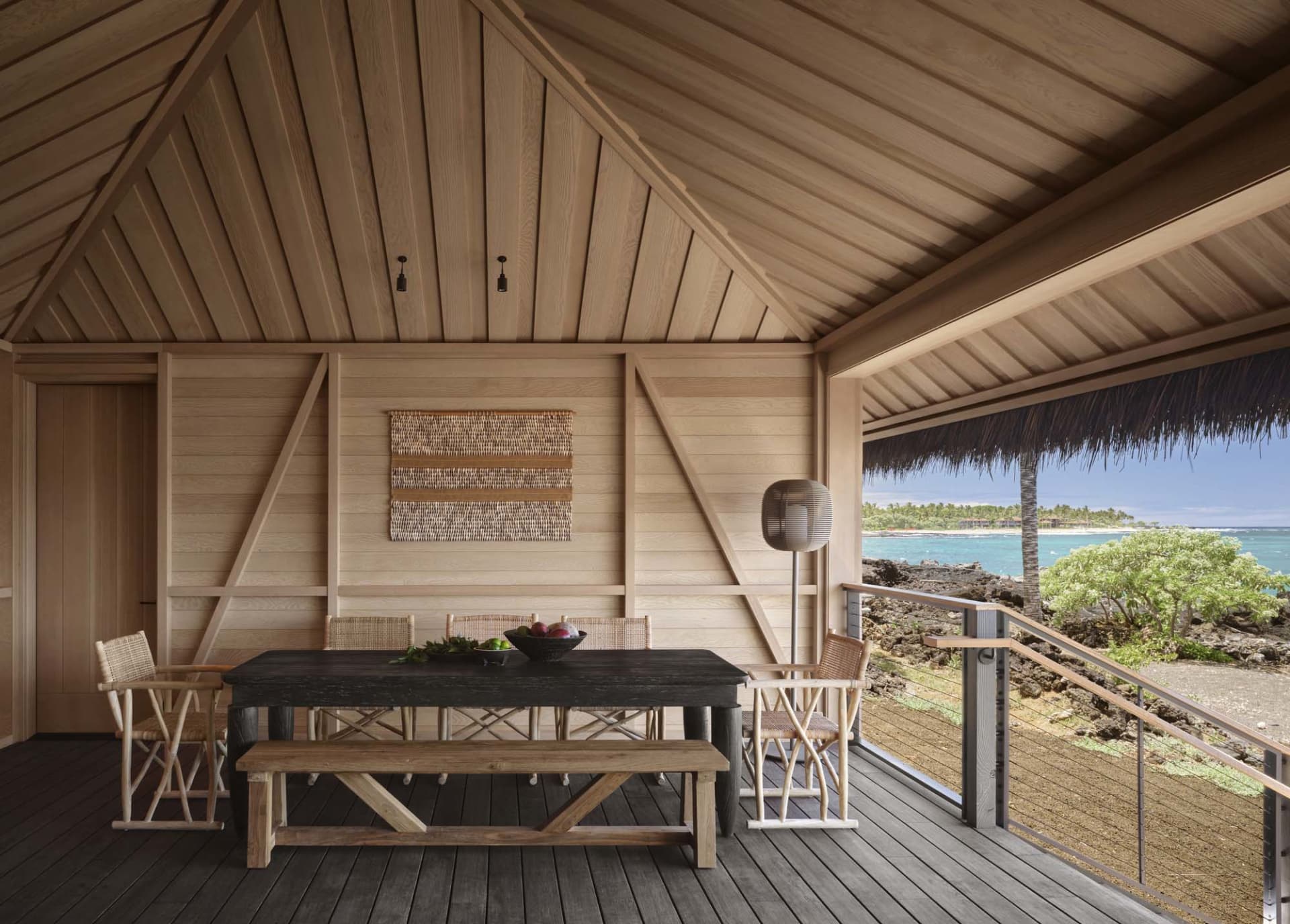 A wooden patio table with chairs and rug, ocean view outdoors.