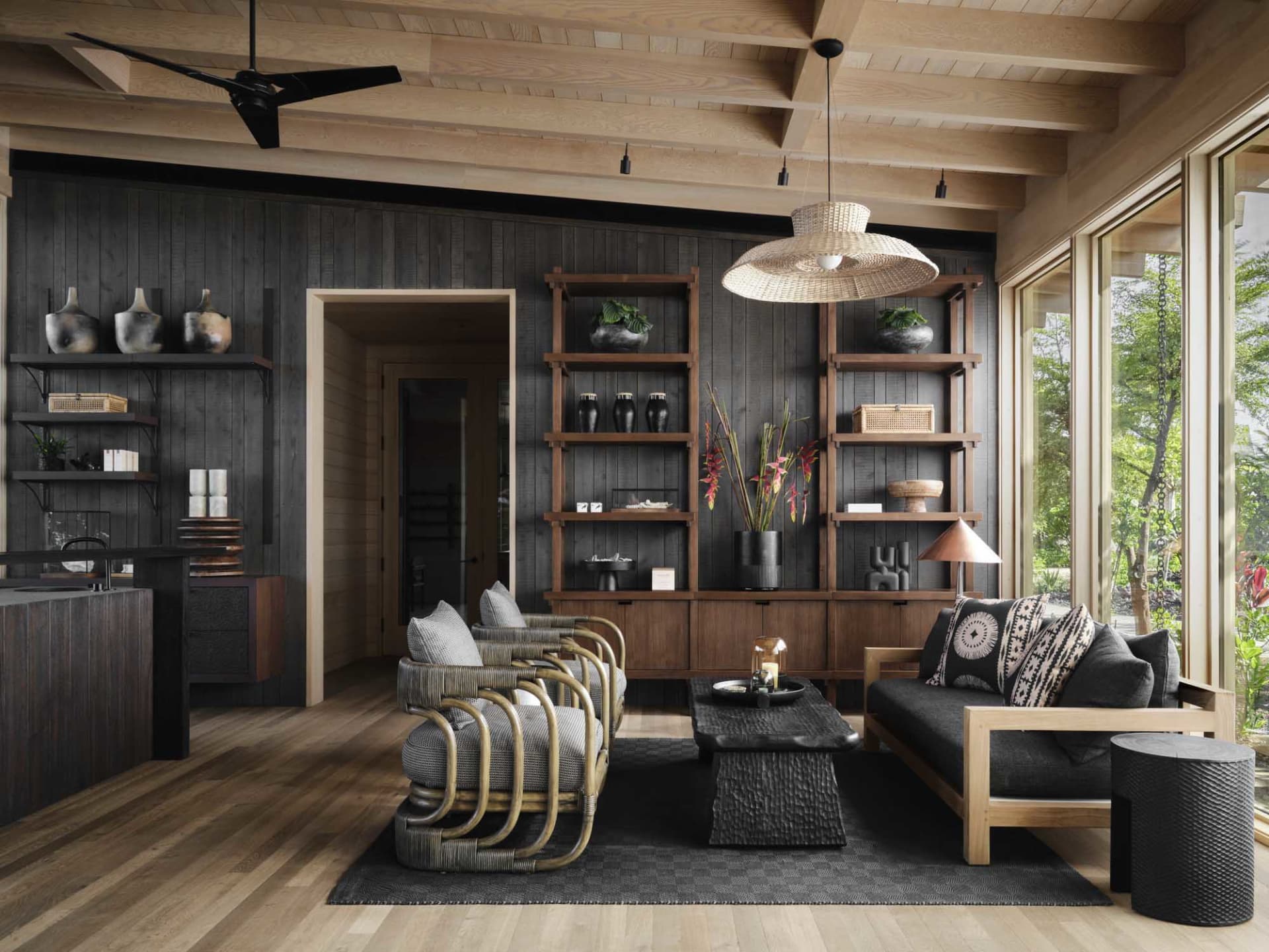 A modern minimalist living room with a wooden floor, black and wooden furniture, and a large window overlooking greenery.