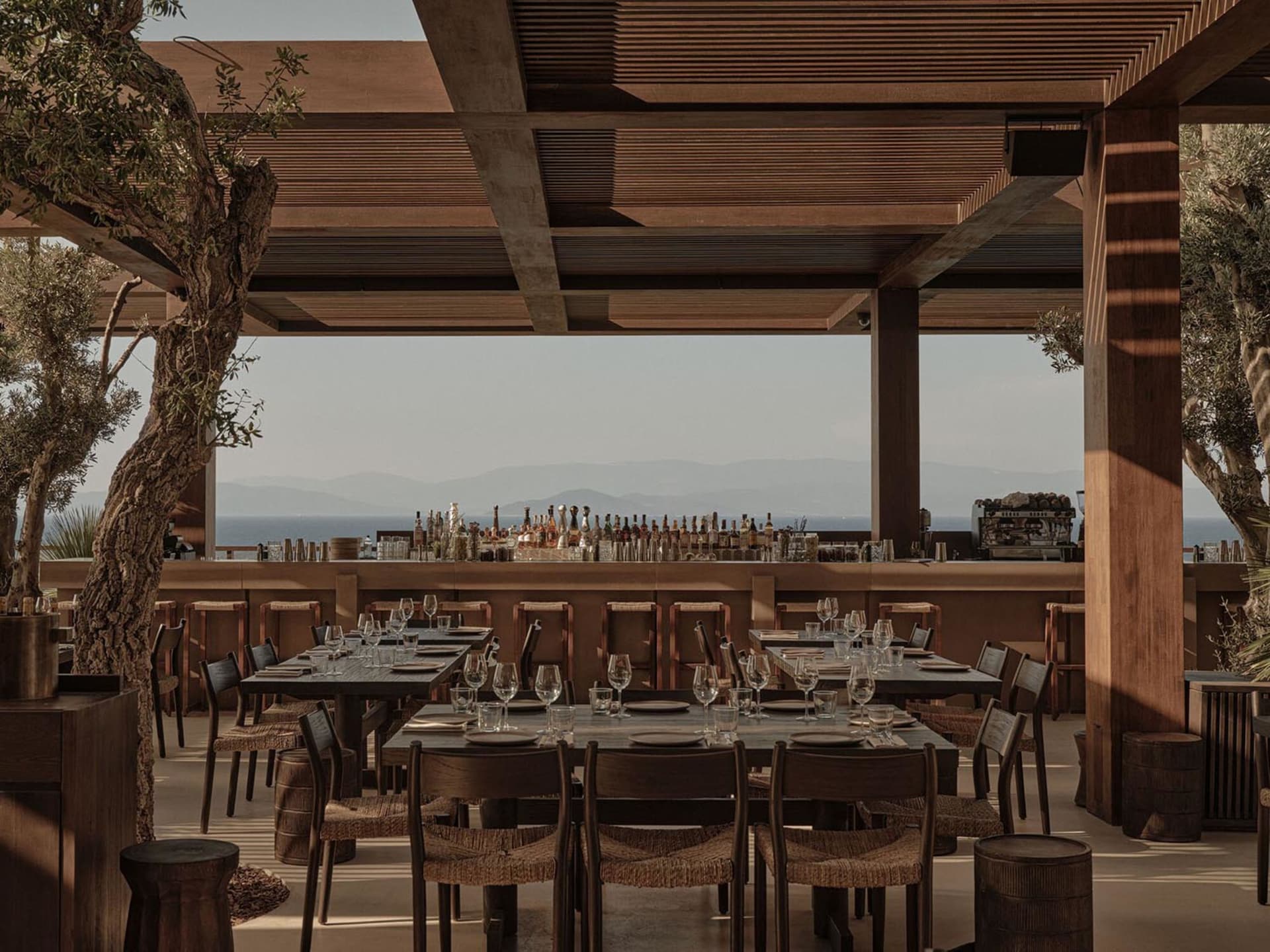 Wooden-furnished dining area with tables set for guests and a bar area in the background.