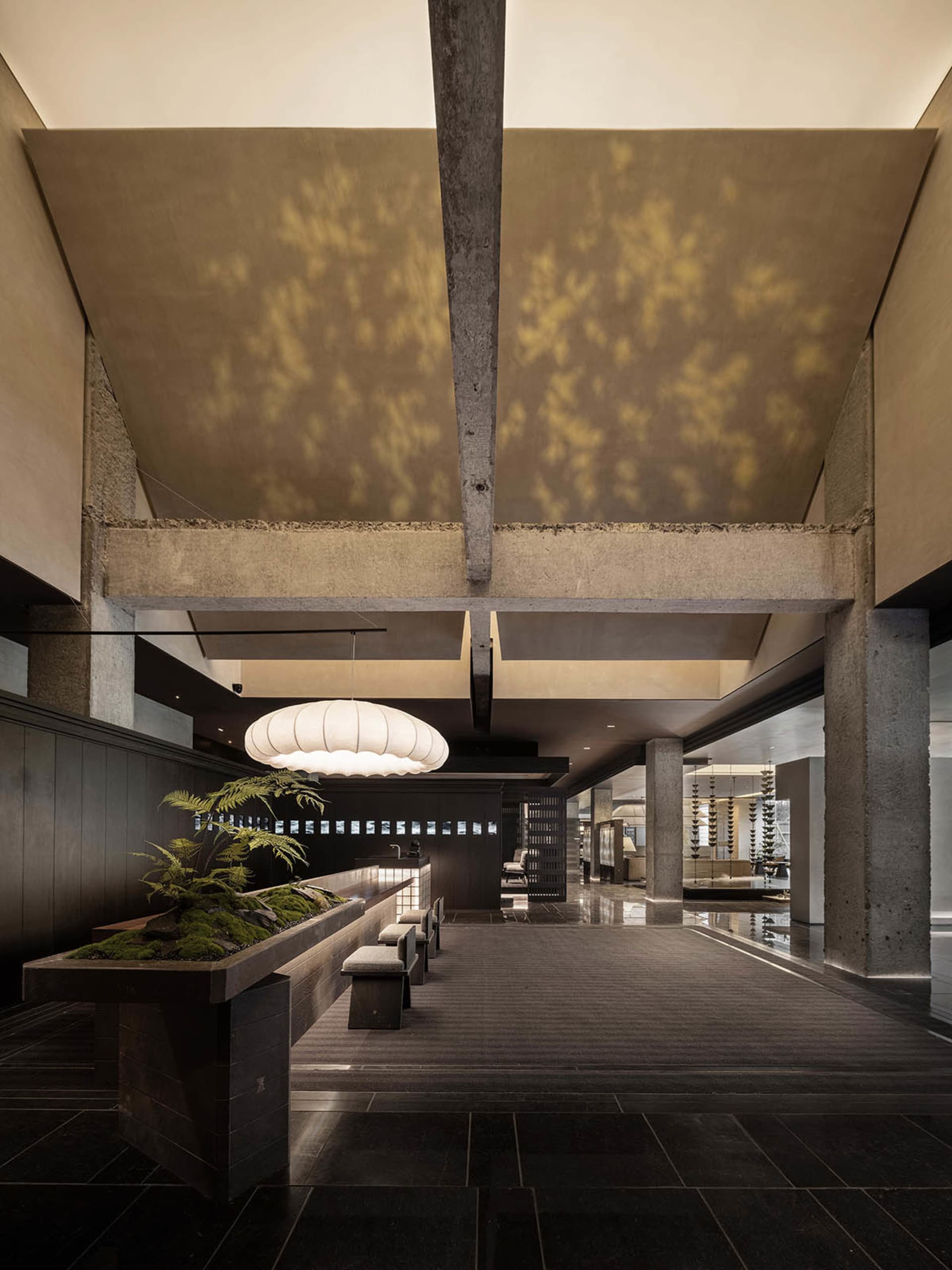 A modern lobby with concrete walls and a high ceiling with exposed beams.