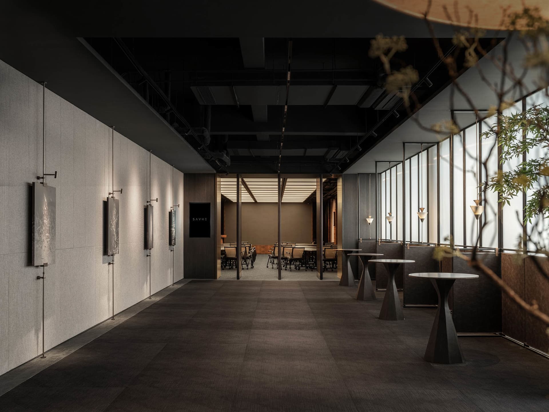 An image of a modern office space with high ceilings, large windows, and high tables, featuring a modern event area with tabl