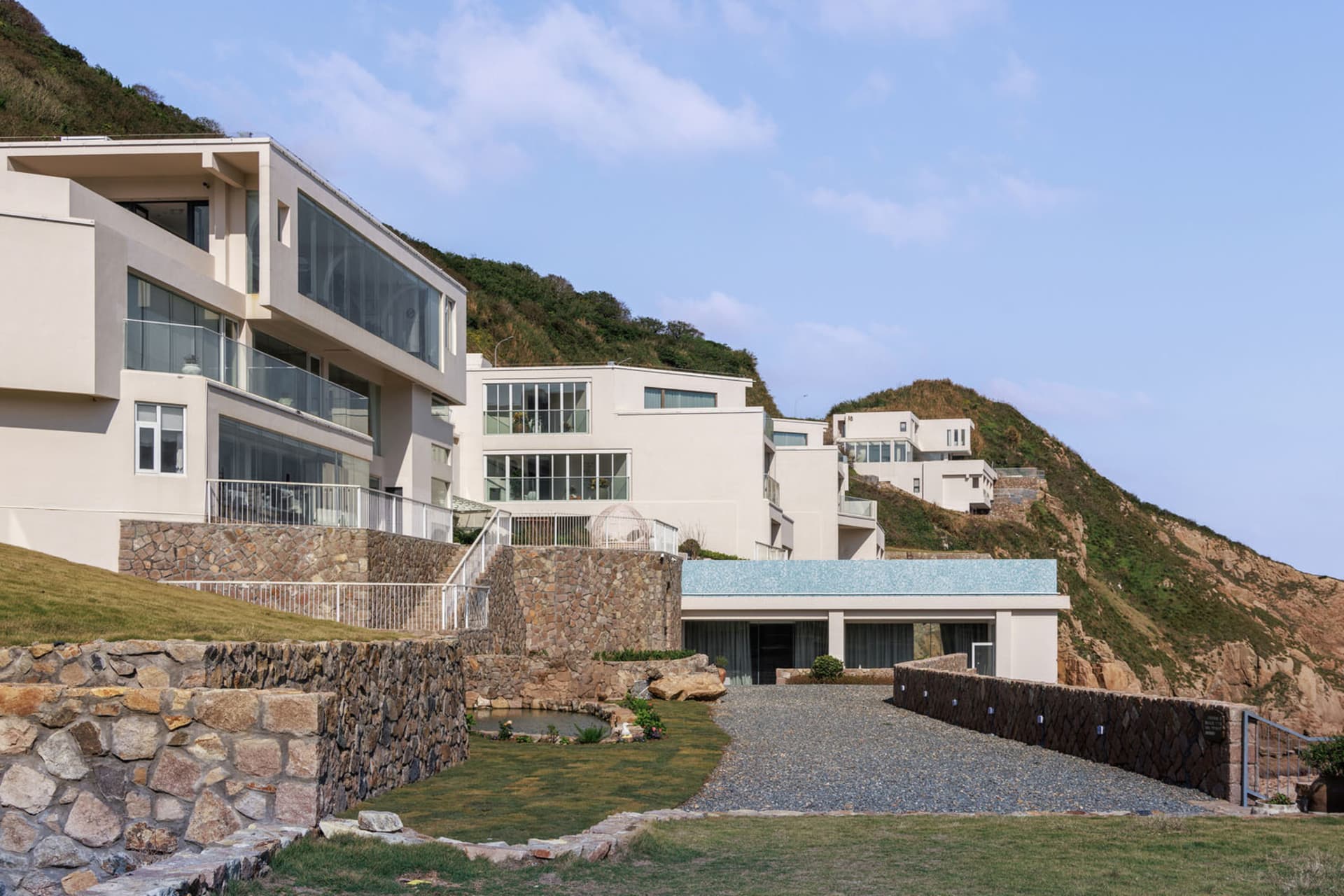 Modern villa house featuring glass walls, stone accents, and concrete structures.