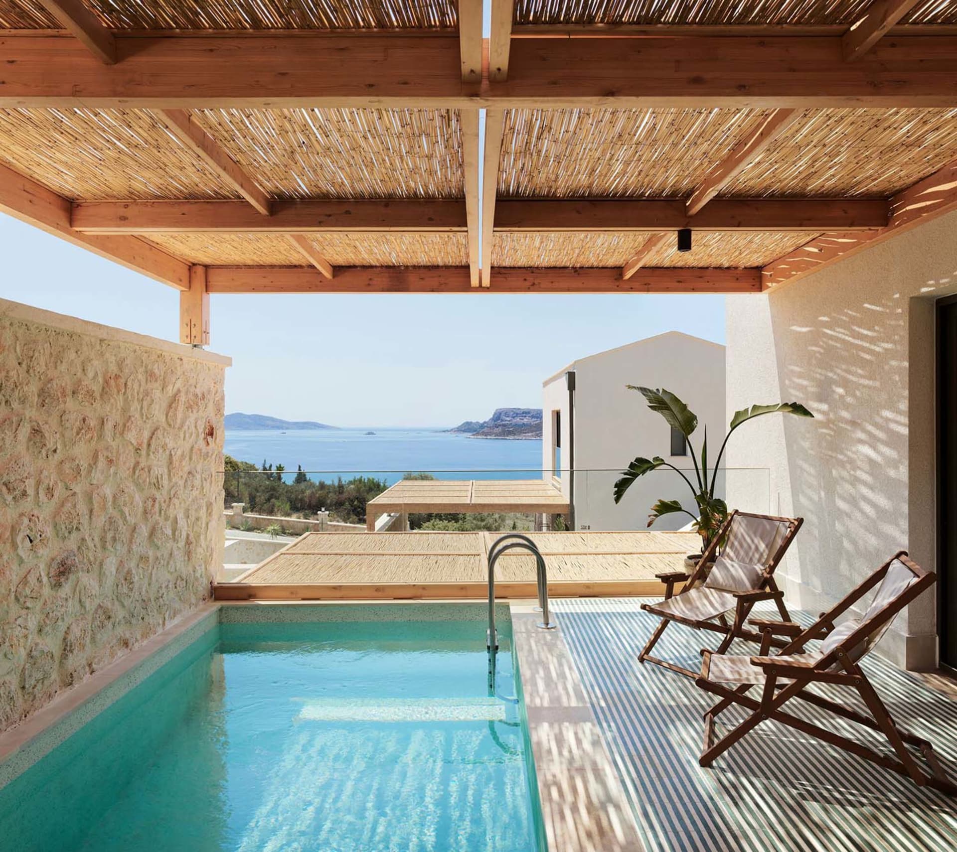 A residential interior featuring a swimming pool with a view of the sea and mountains, covered by a wooden pergola with a tha