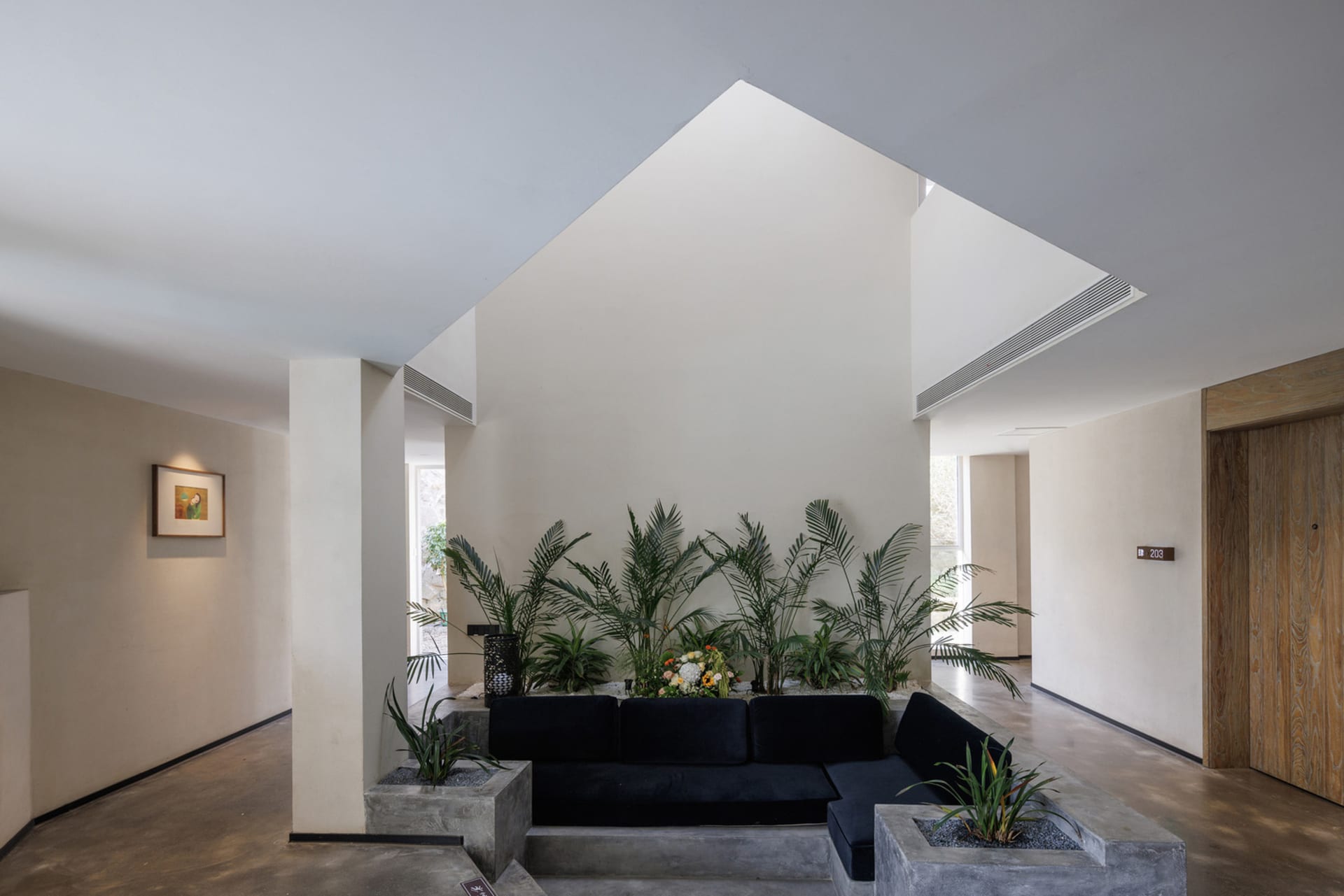 A modern lobby with a concrete seating area surrounded by tropical plants.