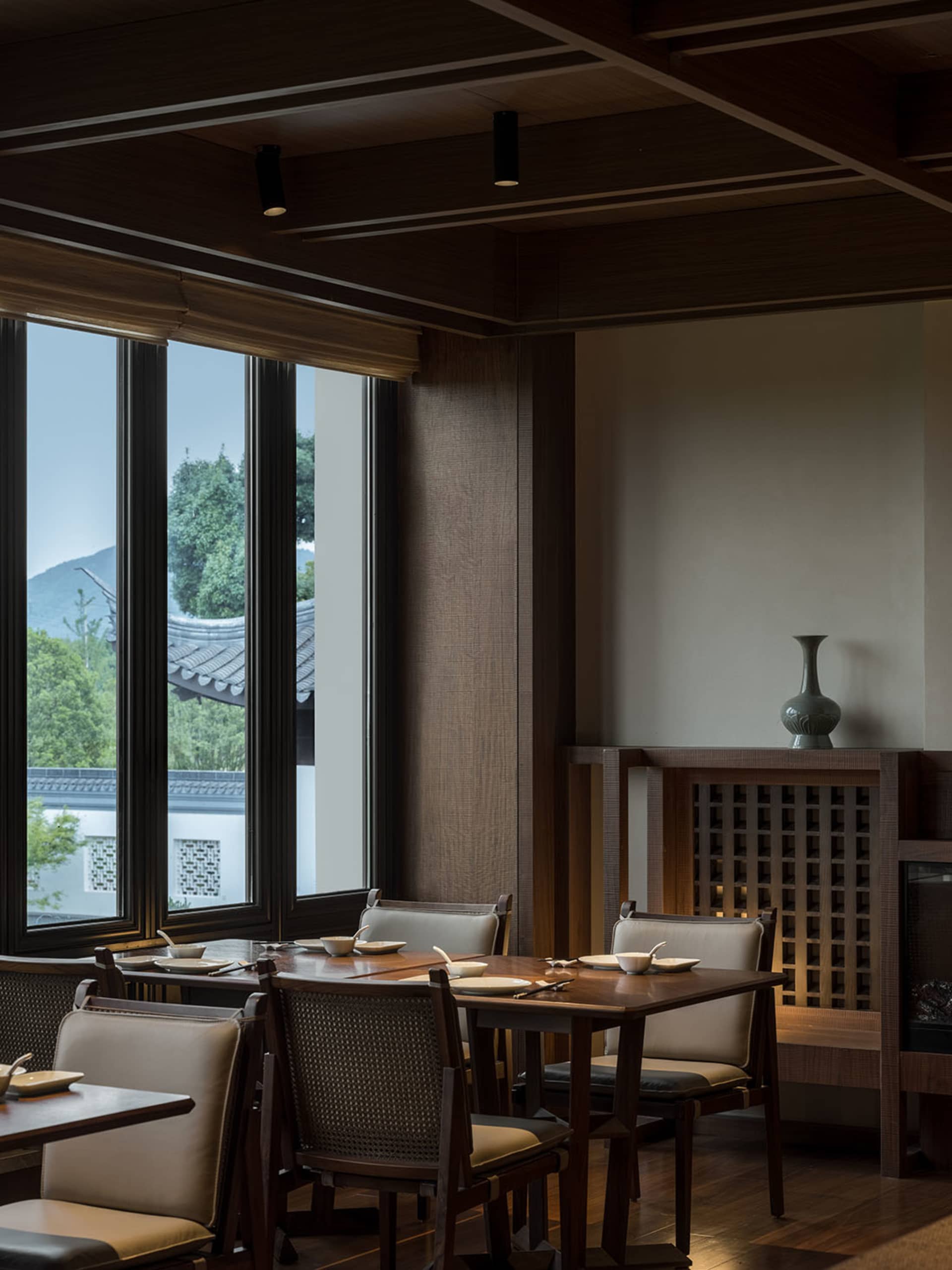 現代餐廳室內，木質餐桌椅搭配大型落地窗，窗外可見山景。